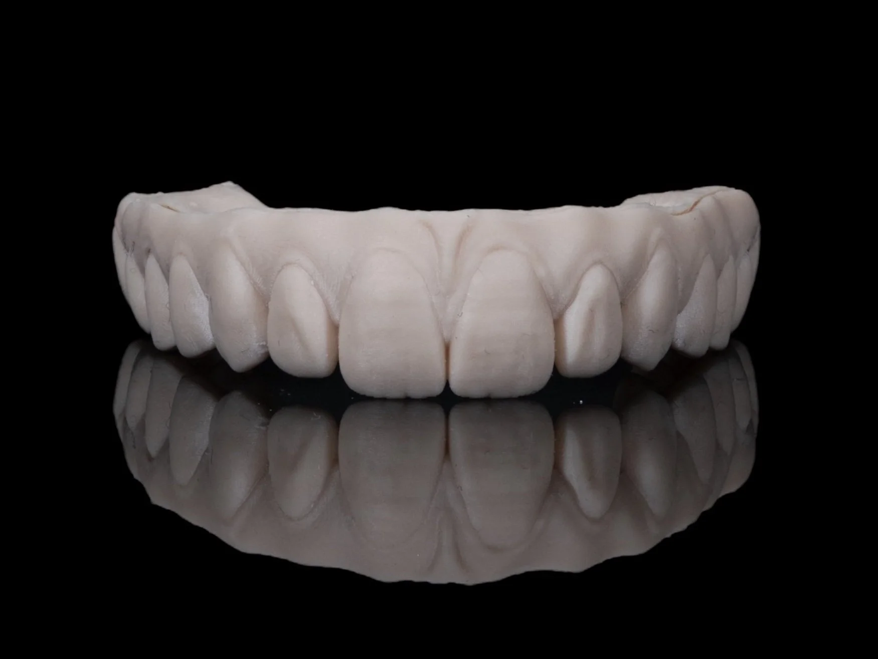 A dental prosthetic model of upper teeth, displayed on a black reflective surface.