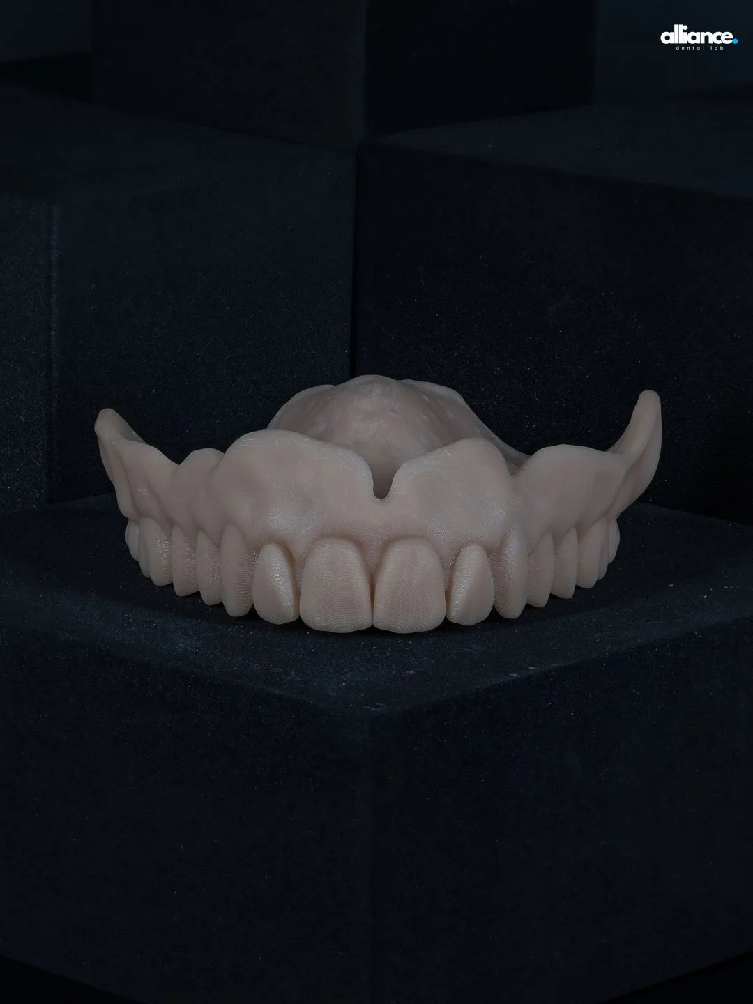 A realistic-looking model of a human jaw with teeth and gums, placed on a black platform with a dark background.