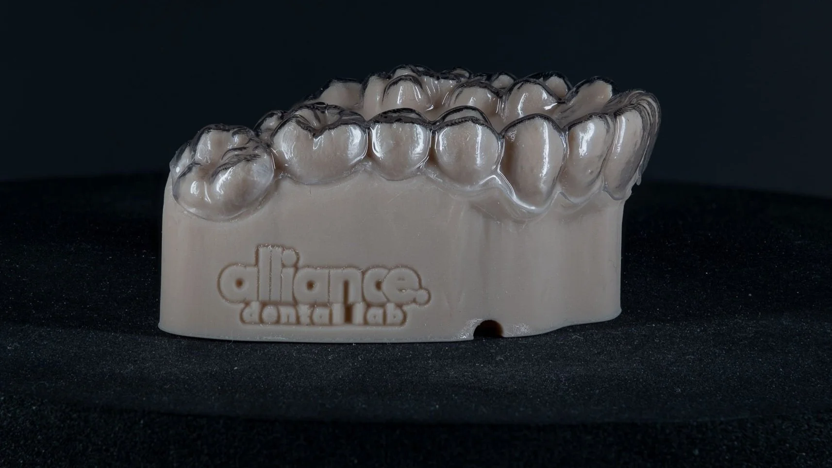 Dental appliance with transparent dental crowns on a white base, labeled 'dlace' with 'dental lab' underneath, placed on a black background.