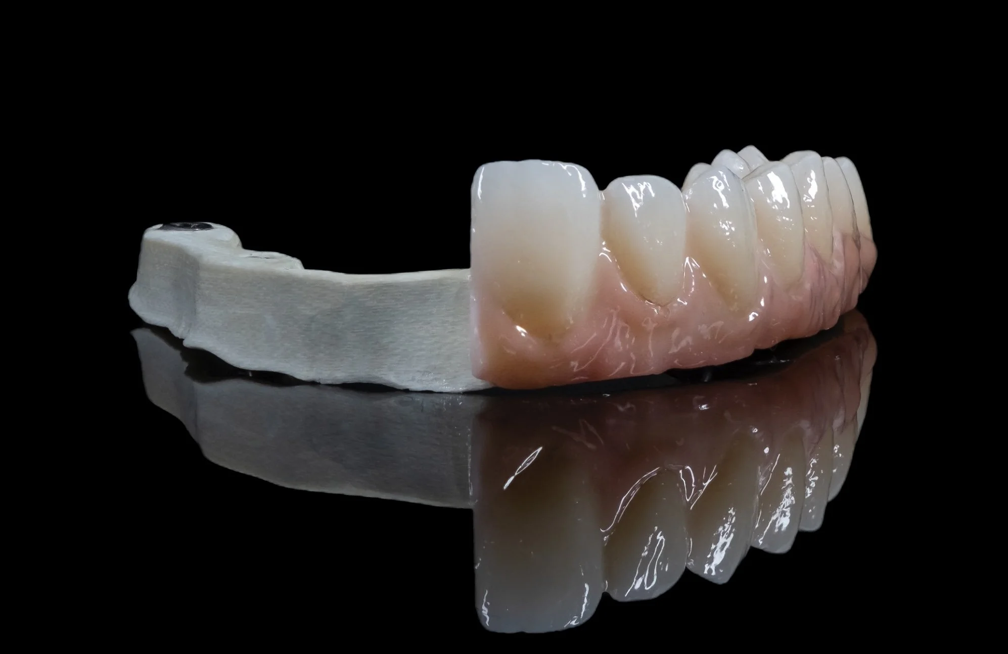A dental prosthetic or denture with porcelain teeth and pink gum material, resting on a reflective black surface.