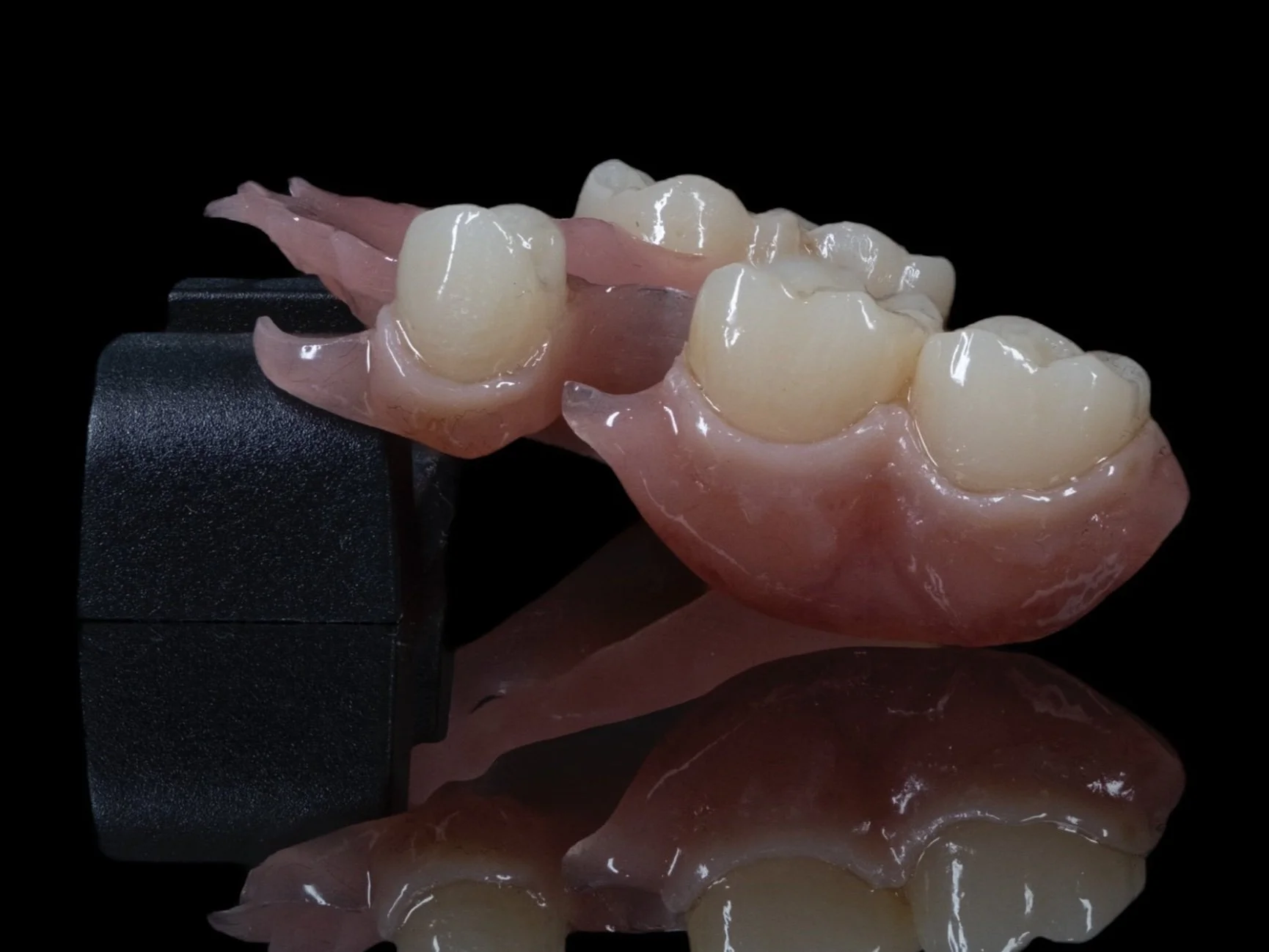 A set of artificial dental crowns and pink gum models on a black background with a reflection underneath.