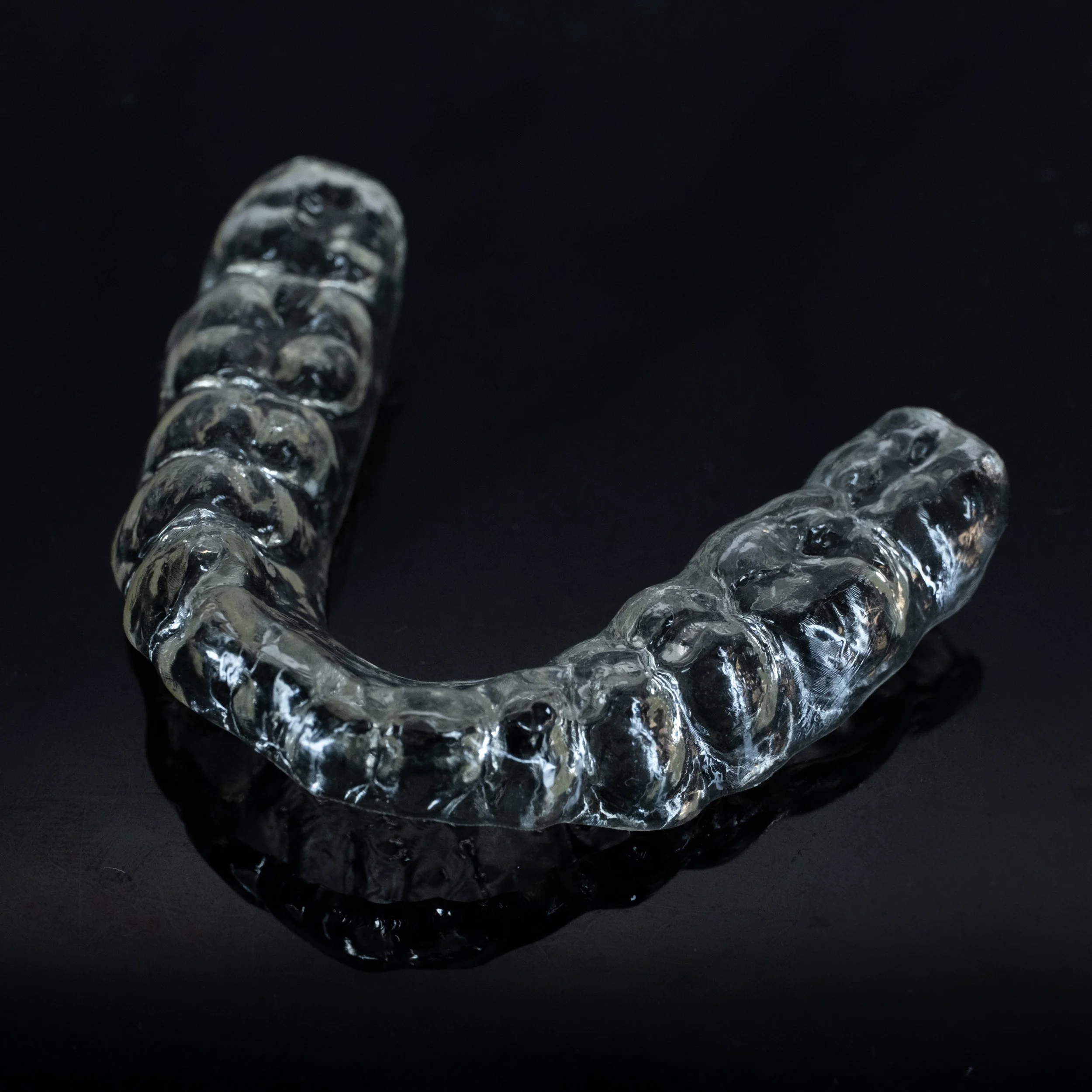 A clear, curved dental aligner resting on a black surface.