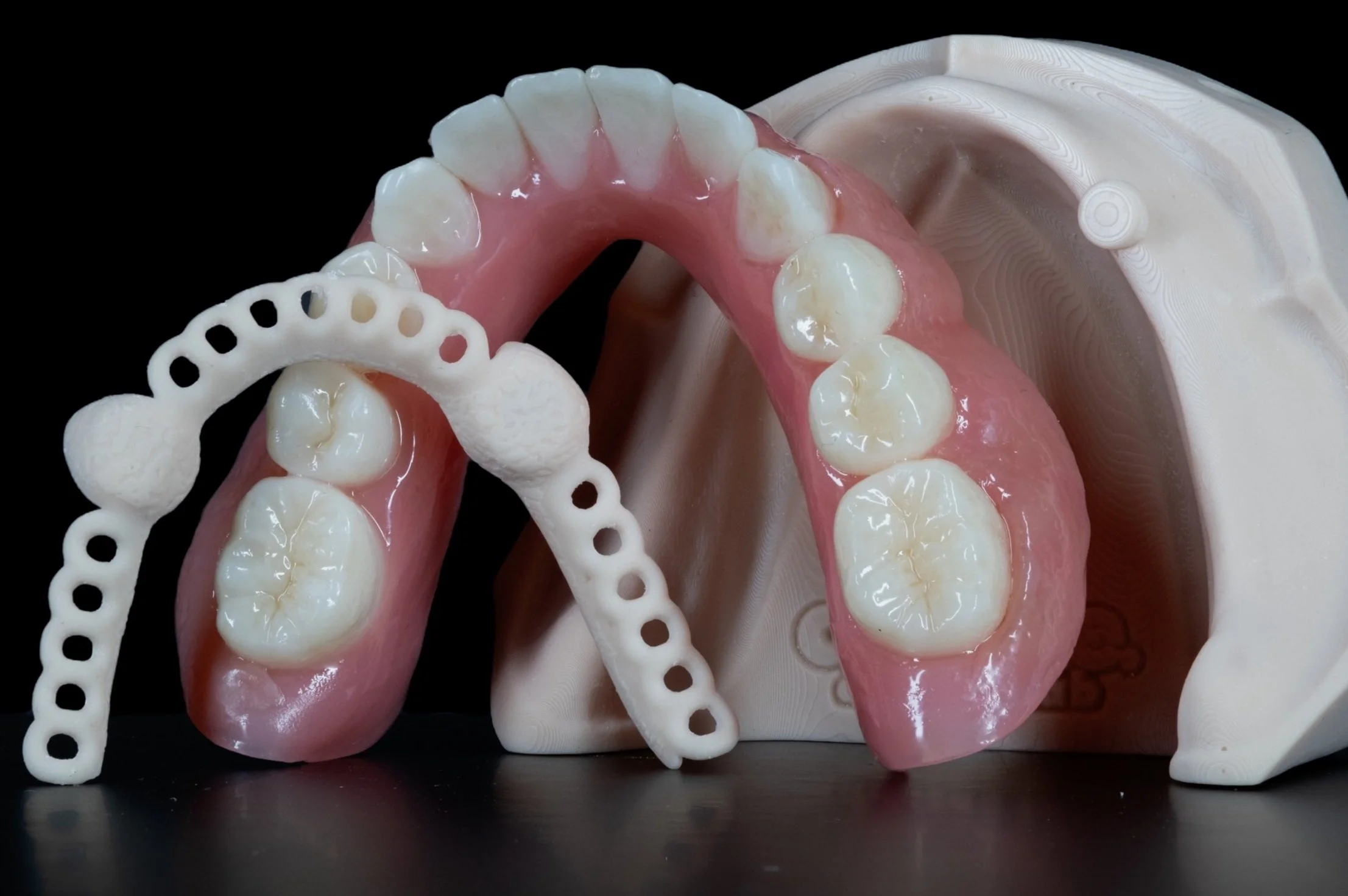 Dental prosthetic models, including false teeth and partial denture frameworks, on a black background.