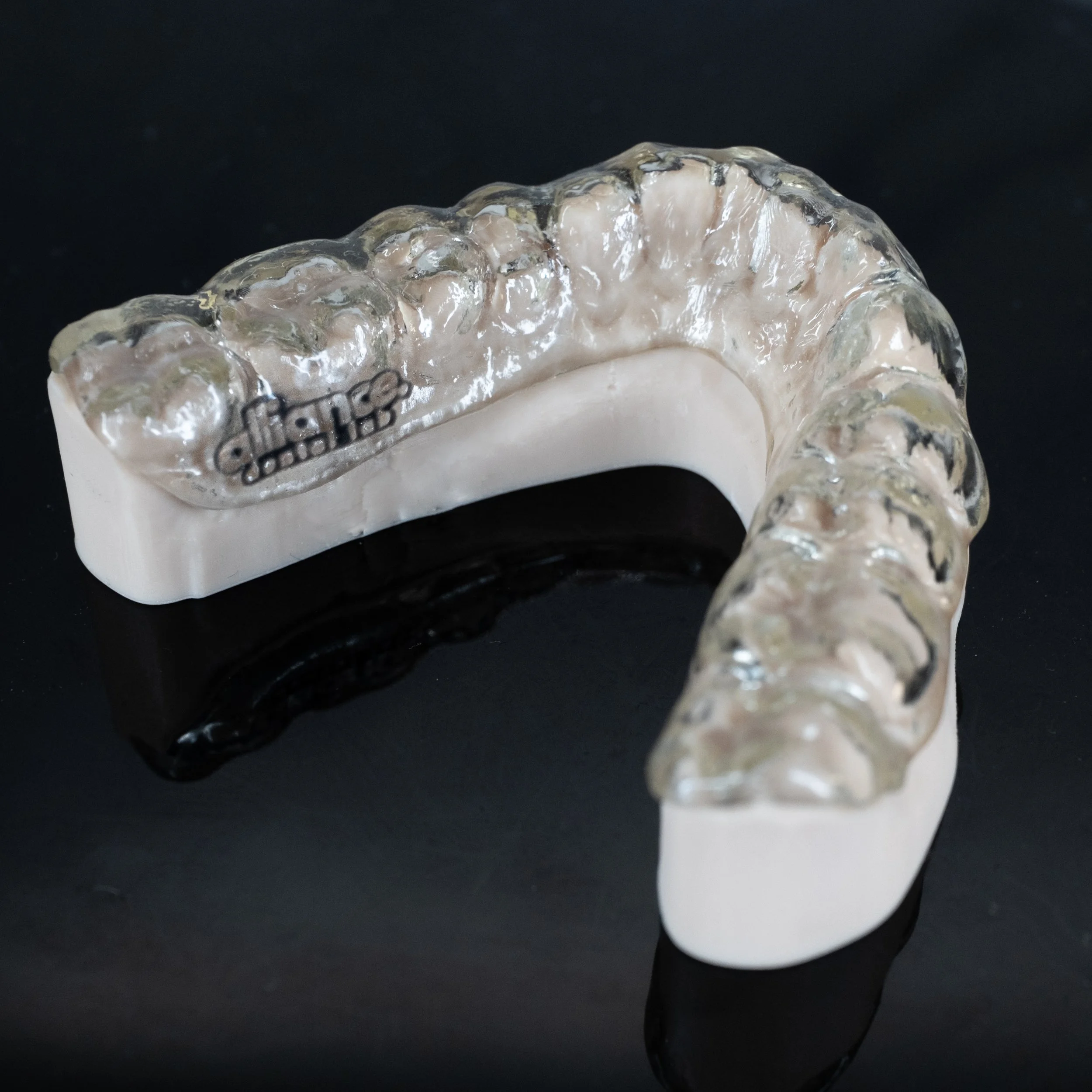 A transparent dental retainer placed on a white base, with reverse text reading 'Glide' on the surface, against a black background.