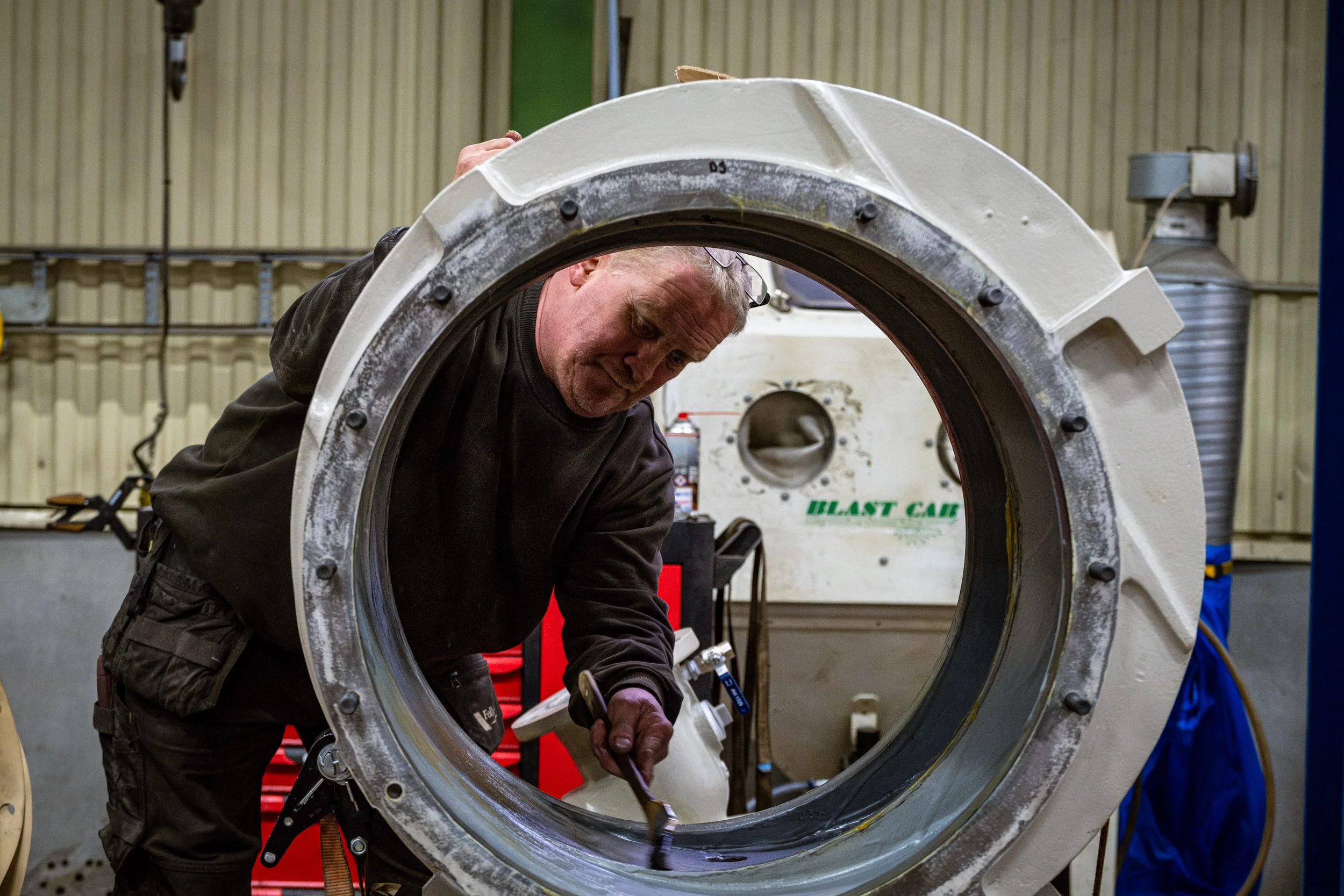 A man working on a large mechanical component in a workshop, using a brush to seal the part.