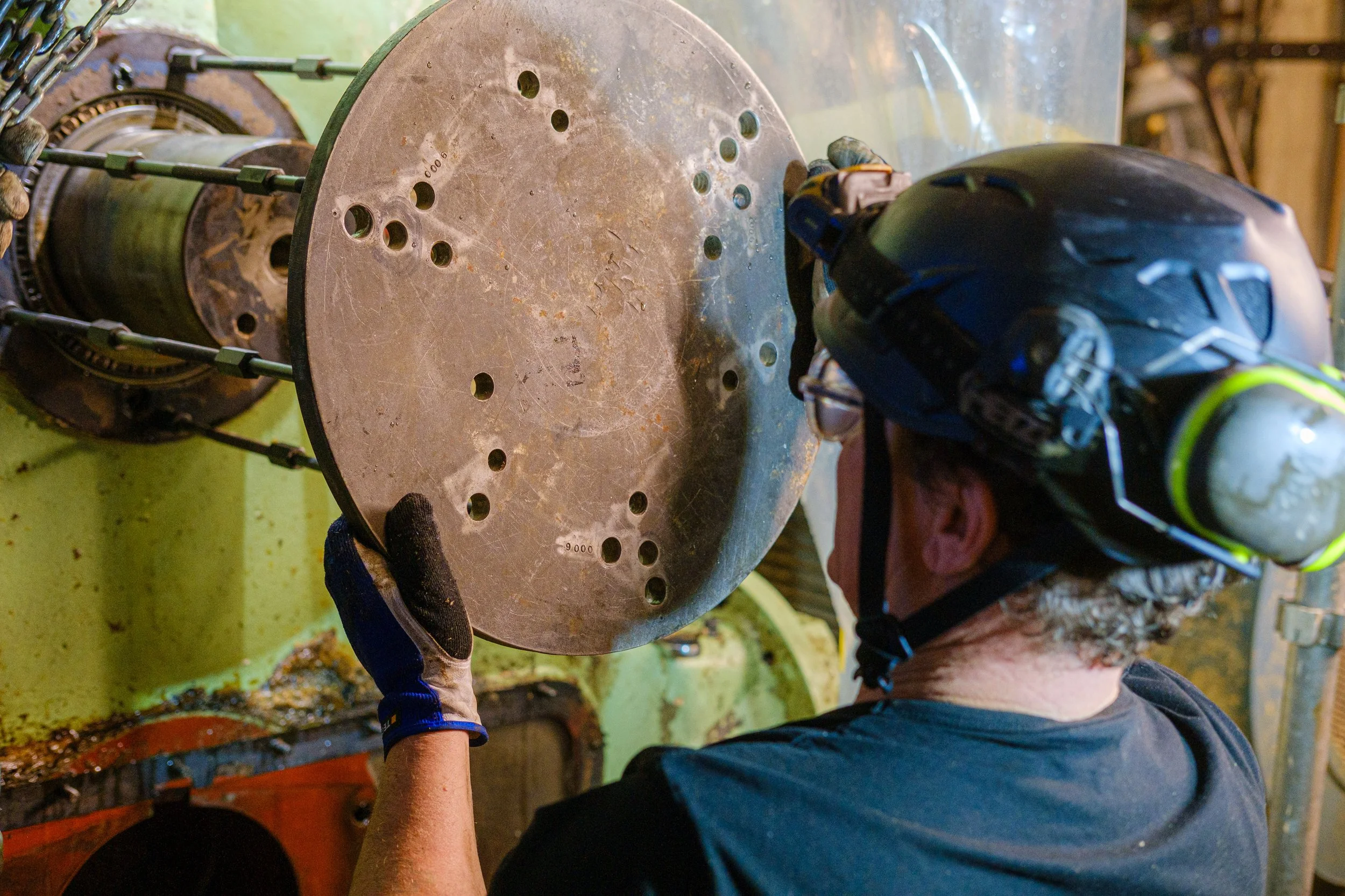 A worker wearing repairing a large industrial component of a vacuum pump part, in a workshop or factory.