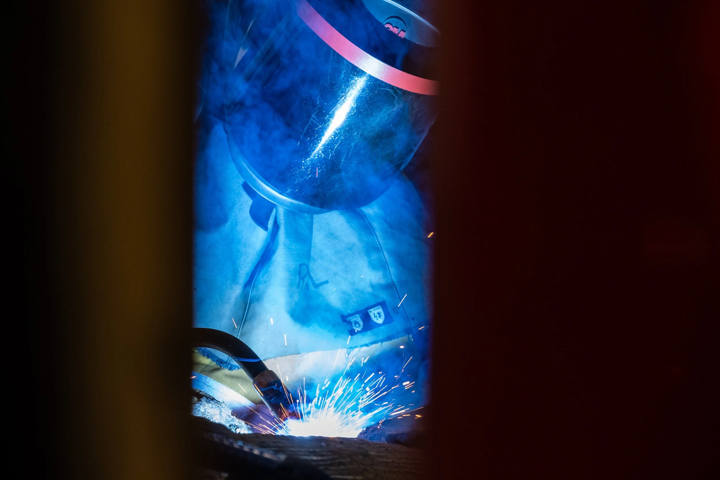 A person welding metal, with blue light glow and sparks flying in a dark environment.
