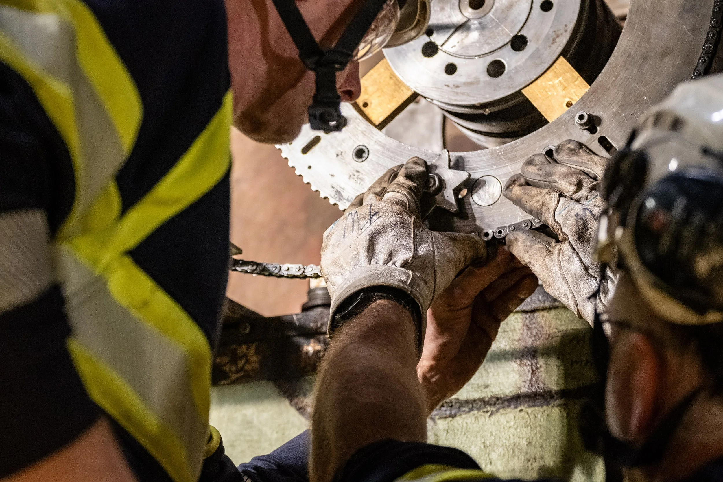 Two workers, wearing gloves and safety gear, are assembling or repairing a large mechanical component.