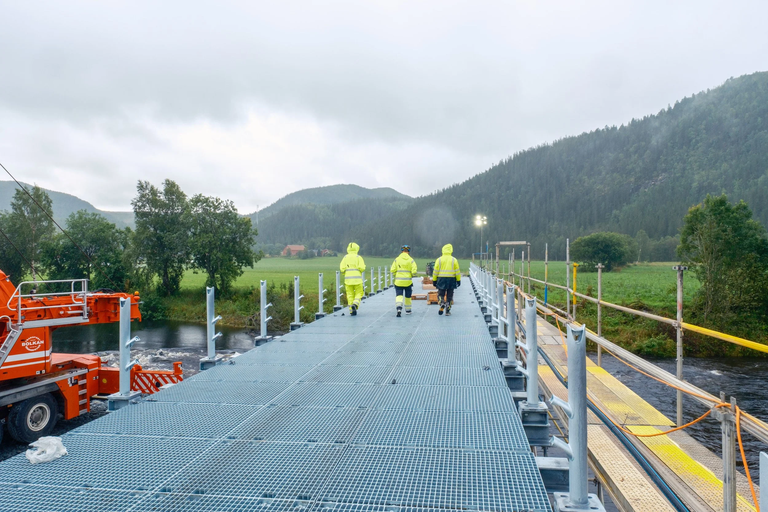 Tre medarbeidere fra Folla Tech går over den nye Breivold bru i Åfjord. Bildet viser gitterristdekket, rekkverksstolper og anleggsarbeid langs brua.