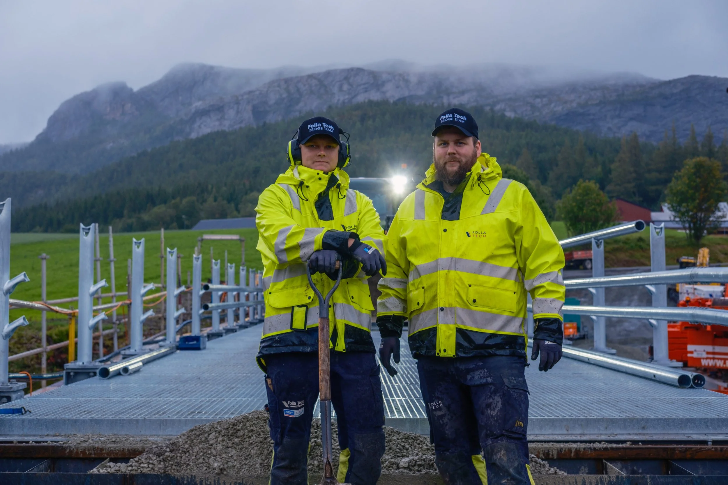 Mathias og Joakim fra Folla Tech står på den nye Breivold bru i Åfjord, iført gult synlighetstøy, med gitterristdekke og brurekkverk i bakgrunnen.