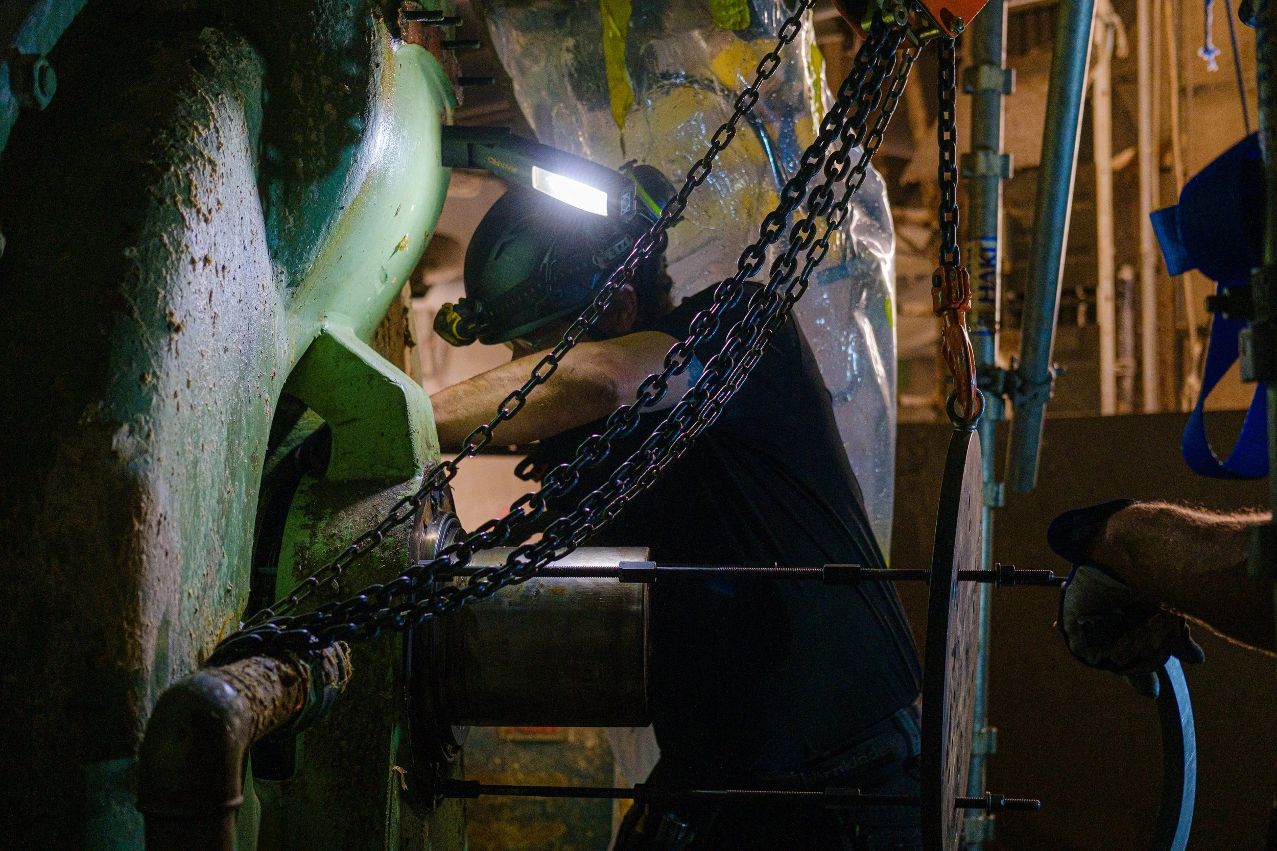 A person wearing safety gear, including a helmet with a headlamp, is working on a vaccum pump.