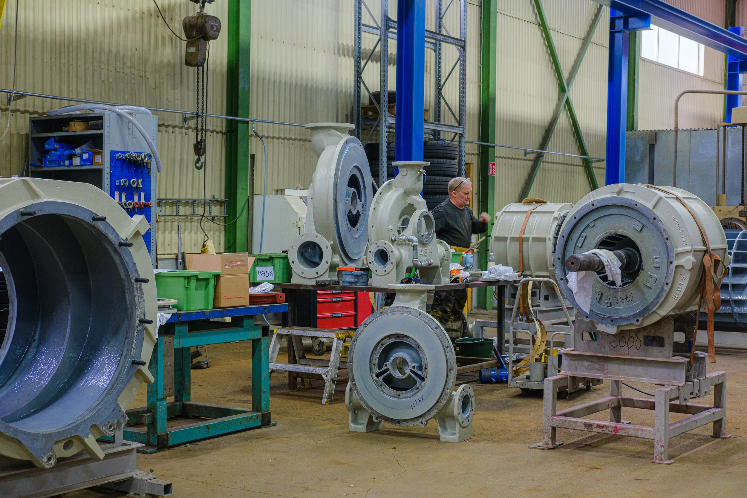 A man working in an industrial manufacturing workshop with large machinery parts, tools, and equipment around him.