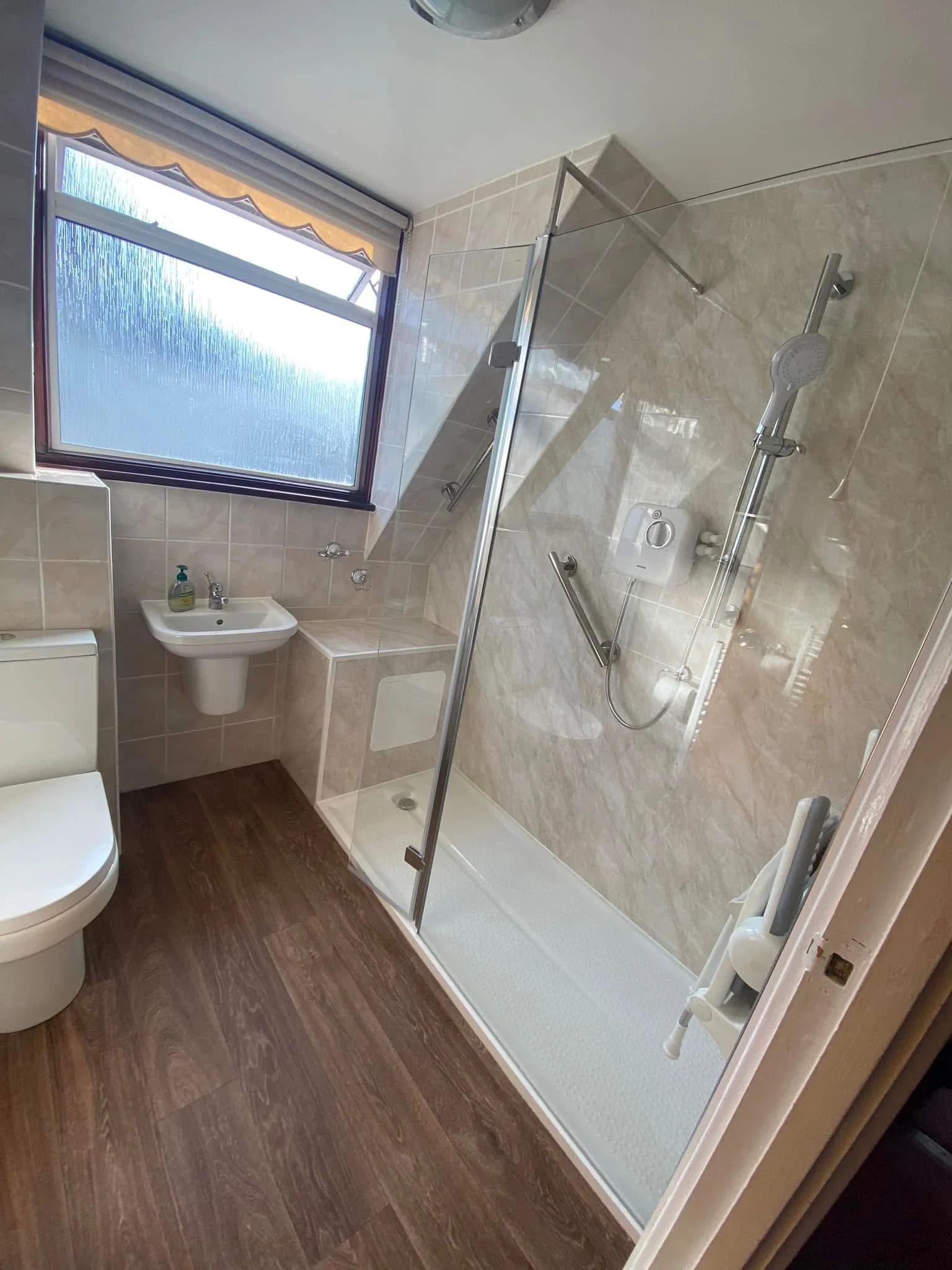 Bathroom with a walk-in shower, a small sink, a toilet, a window, and brown wood-patterned flooring.
