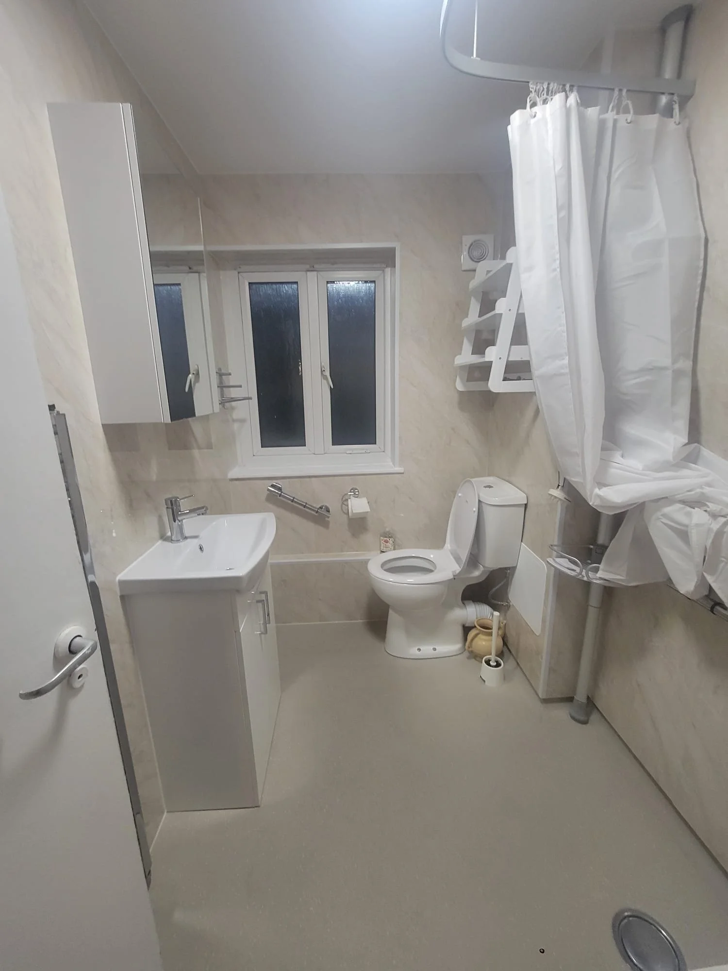 A small bathroom with a toilet, sink, window, and shower with a curtain, all in neutral tones.