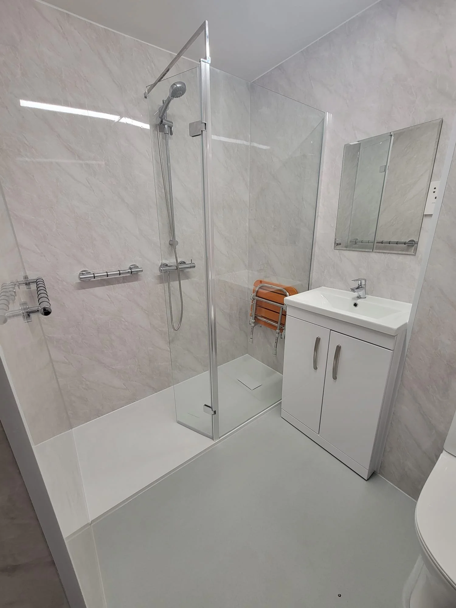 Small bathroom with a walk-in shower, a white vanity with a sink, a mirror, and a folded orange chair stored against the wall.
