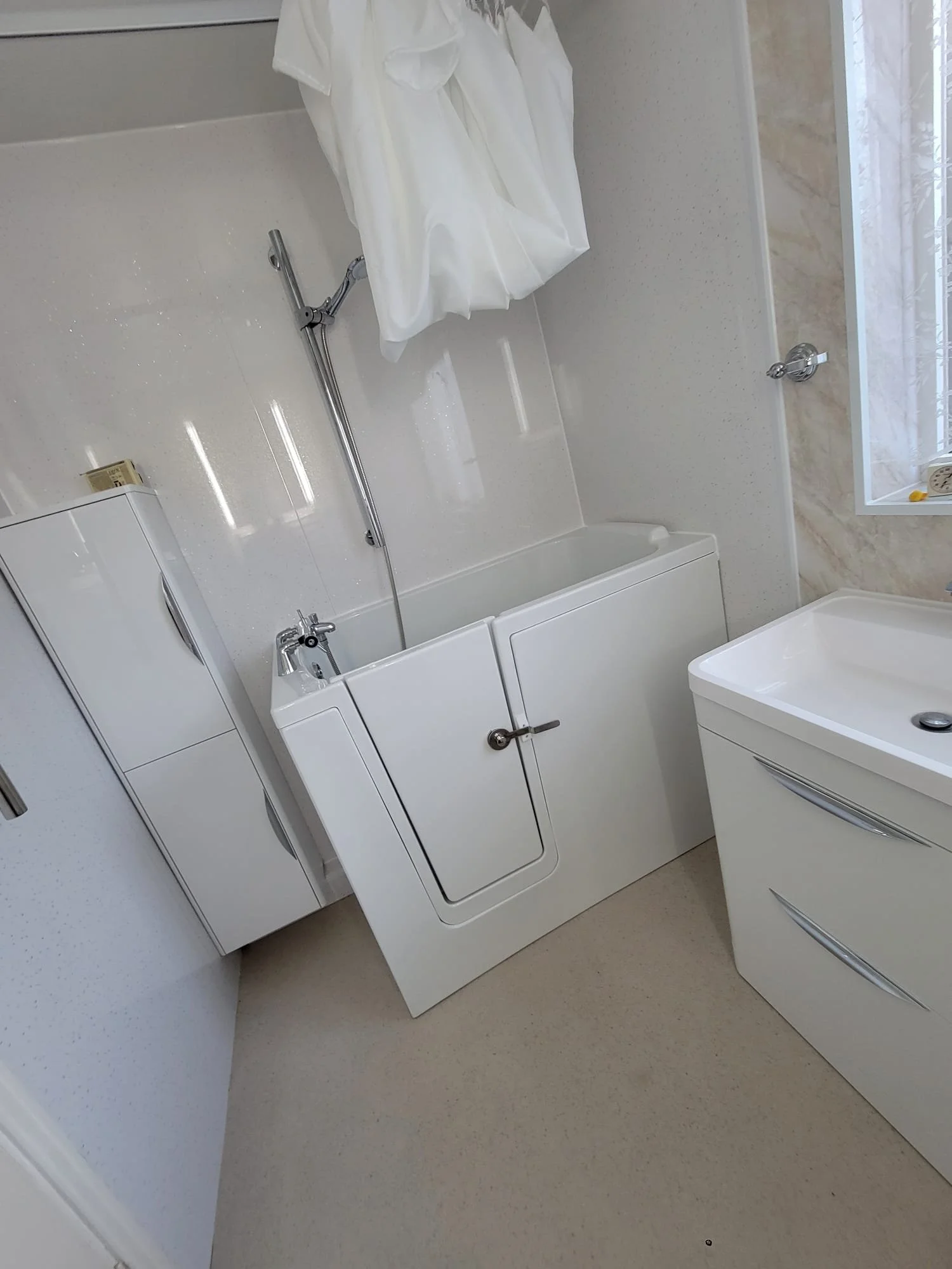 A bathroom with a bathtub, shower head, white cabinet, and a sink with a cabinet, all in neutral tones.
