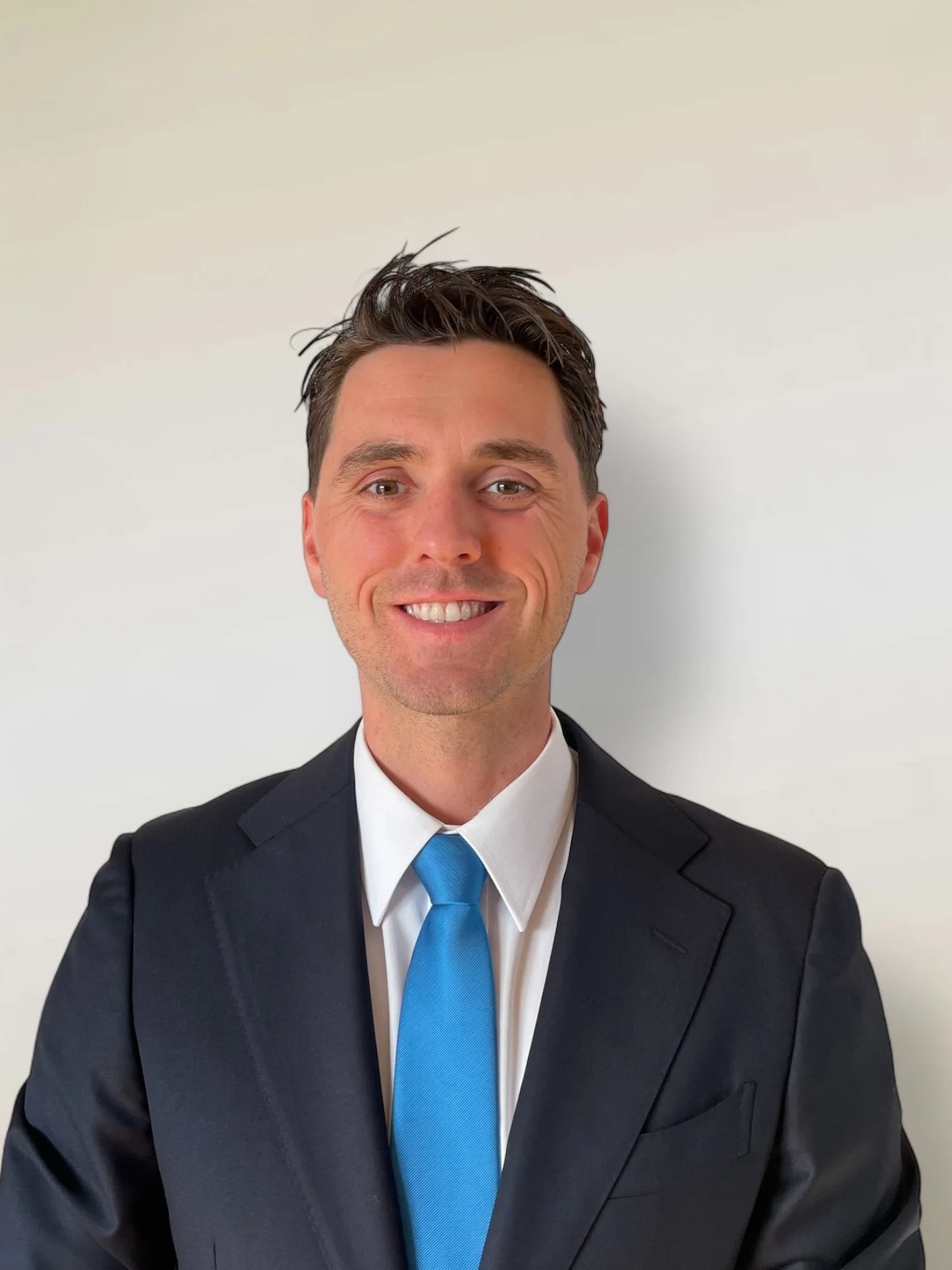 Guus Schrameijer in een grijs pak en stropdas, glimlachend, tegen een neutrale achtergrond.