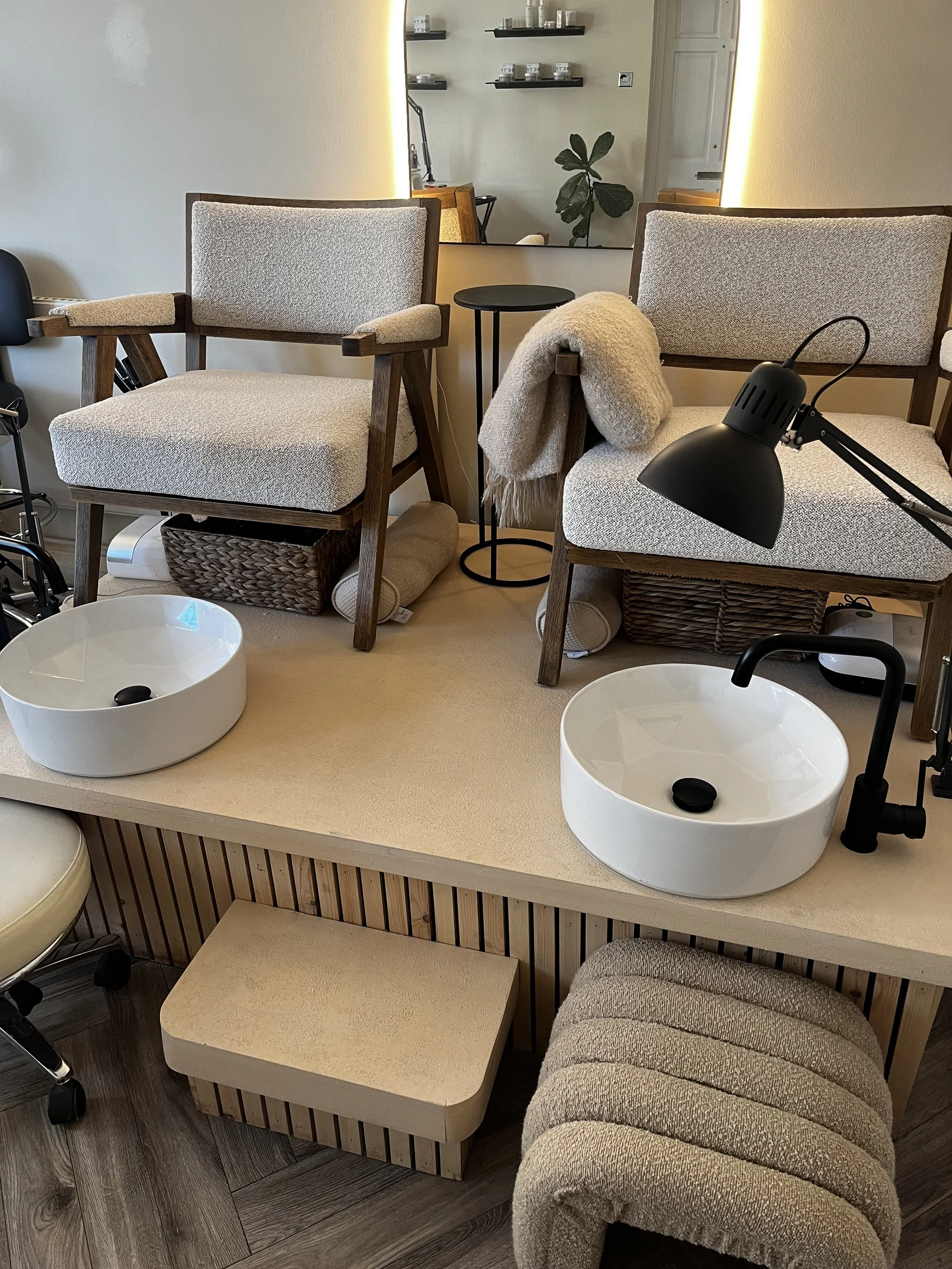 Modern pedicure station with two white cushioned chairs, foot basins, a small side table, and ambient lighting.