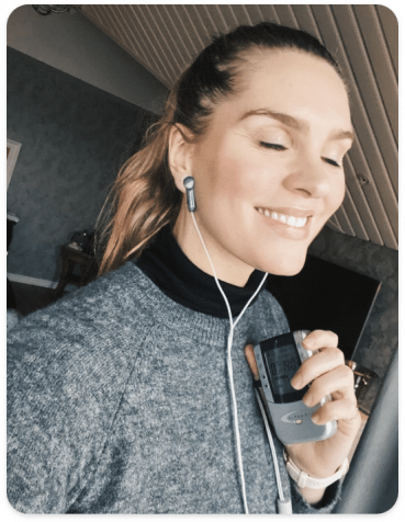 A woman with closed eyes smiling while holding a walkie-talkie and wearing earphones.
