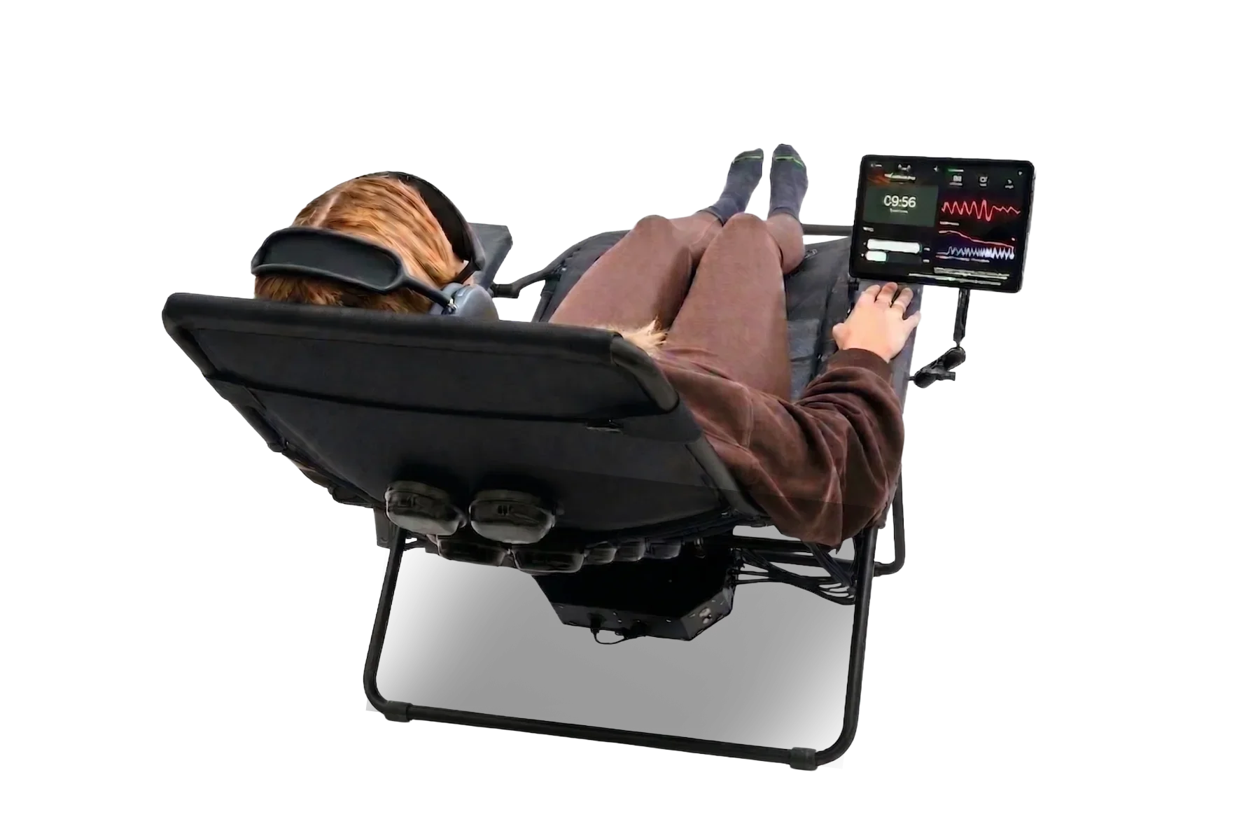 Person lying on a recliner chair with a headset, using a tablet that displays heartbeat and brainwave graphs.