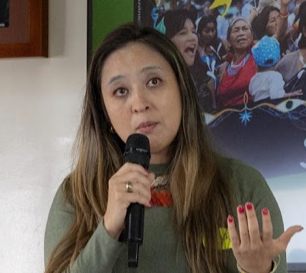 Retrato de una mujer con cabello negro y camiseta de rayas blancas y azules, fondo natural con árboles.
