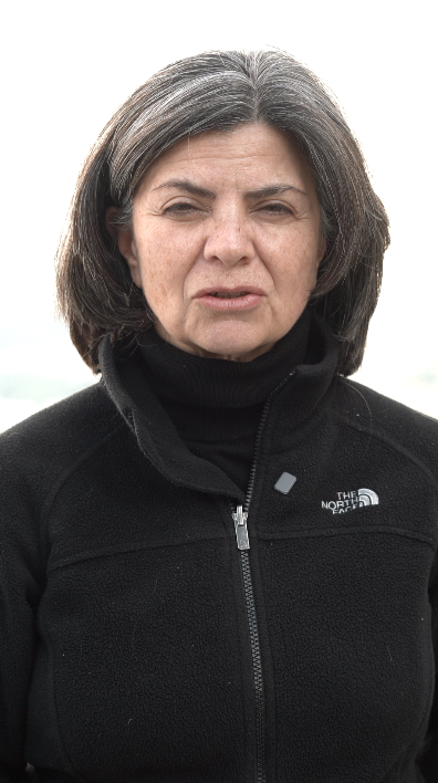 Mujer usando chaqueta negra de The North Face, con cabello corto y canoso, expresión seria, fondo difuso y cielo nublado.