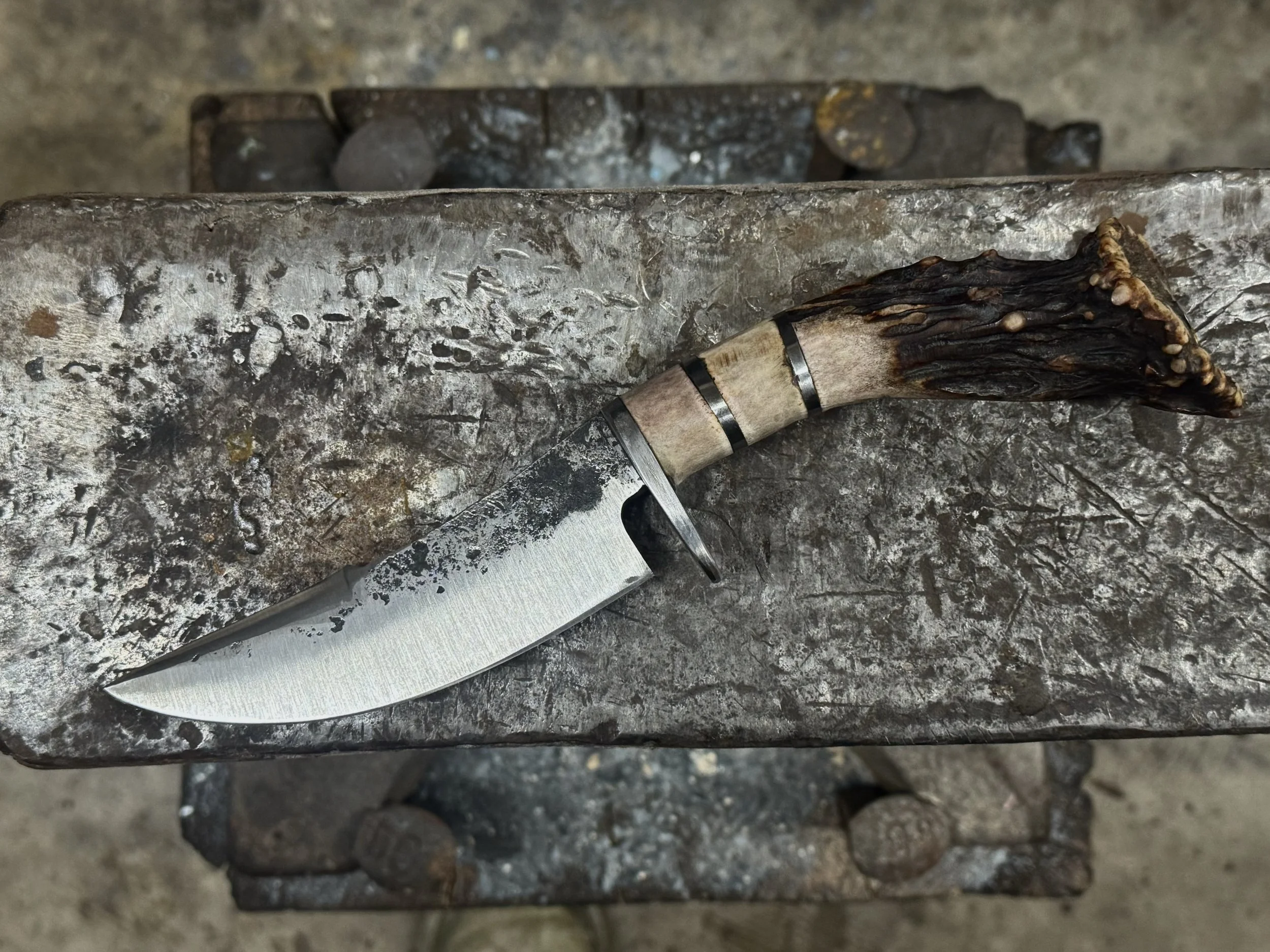 A small knife with a leather-wrapped handle and a weathered blade resting on a metal surface with blacksmith marks.