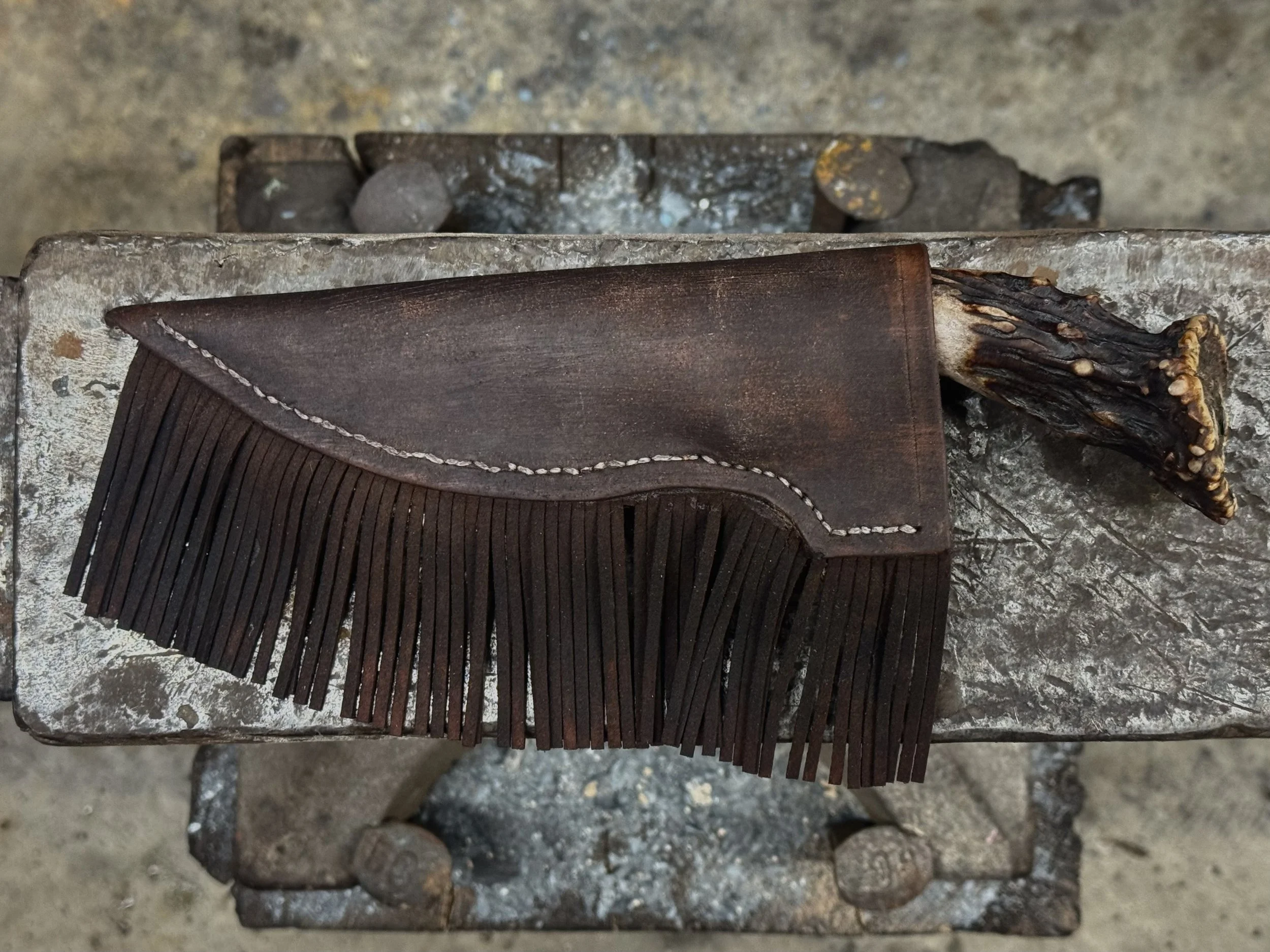 A leather saddle with fringe and a carved wooden handle on top of a weathered metal surface.