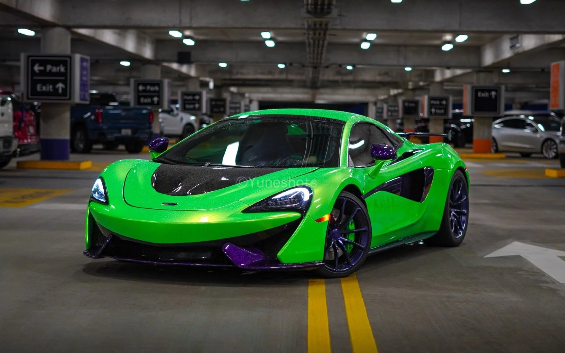 Front view of a custom green 2020 McLaren 570S Spyder with purple forged carbon fiber accents parked in a garage, available for exotic car rental in Tampa, Clearwater, St. Petersburg, and Miami, Florida.