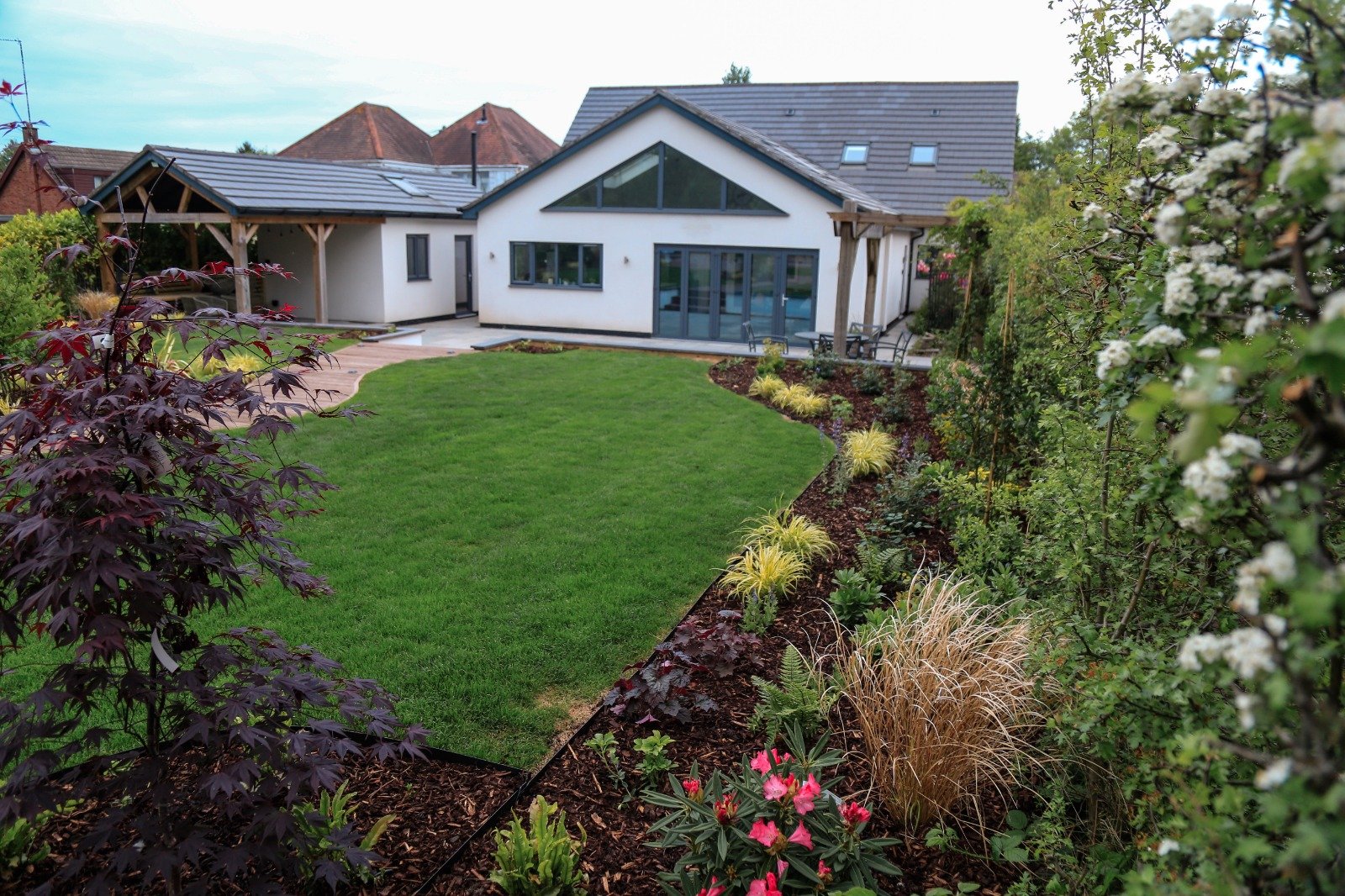Modern house with a well-maintained green lawn and various plants and flowers along the garden edge.