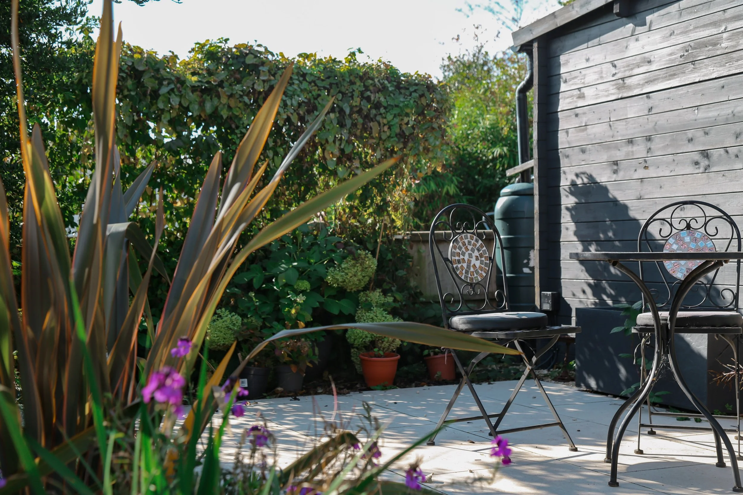 Garden patio area with cream porcelain paving, and outdoor furniture, lush green planting in the background
