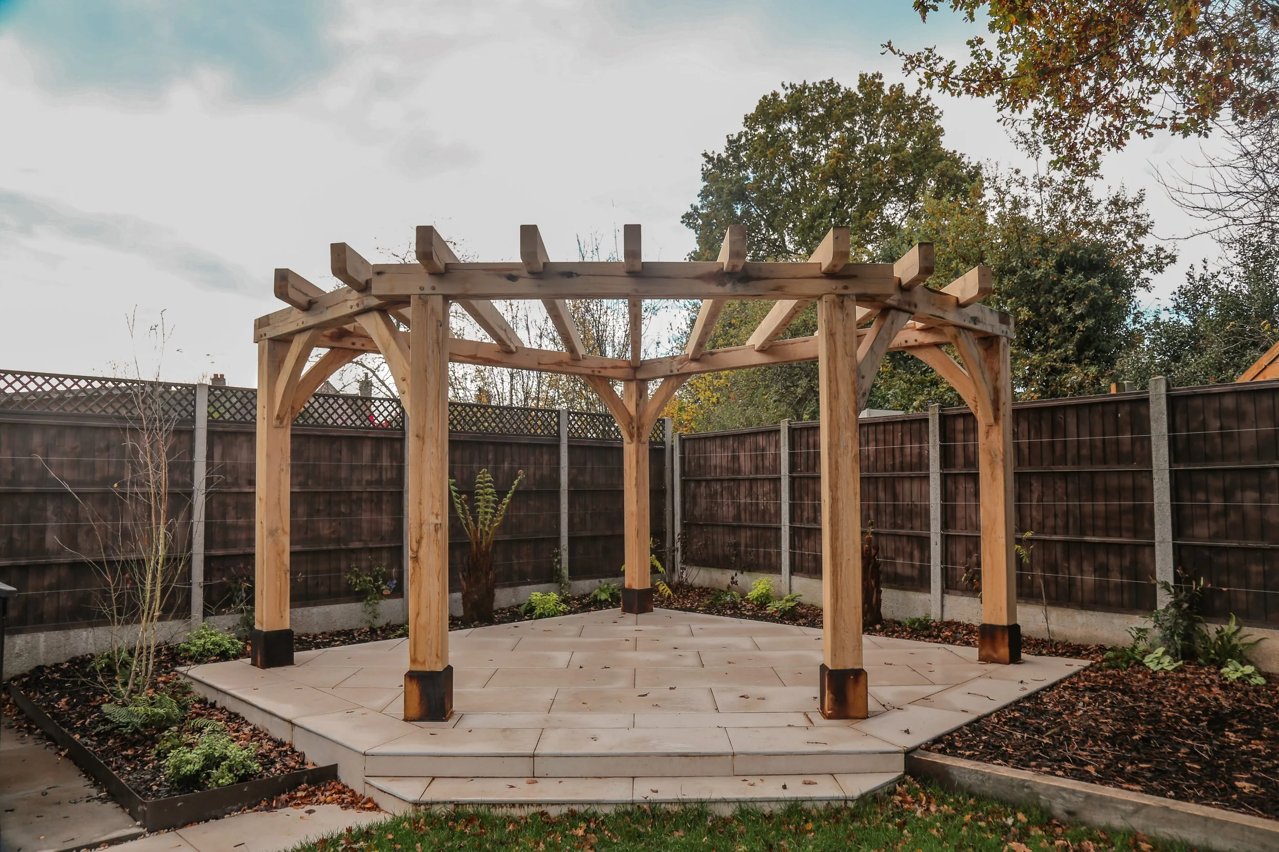 Oak framed pergola sat on a porcelain patio, surrounded by planting beds, Luxury landscaping in Warwickshire