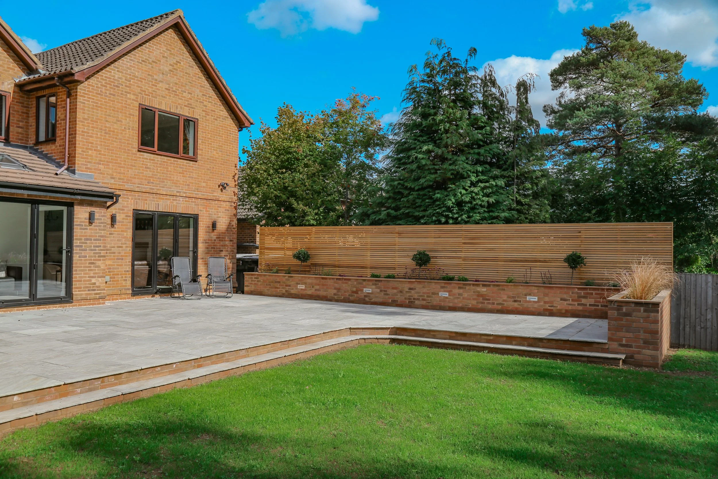 Brick built raised planting bed, natural stone paving and a cedar slat fence, luxury garden landscaping in Warwickshire