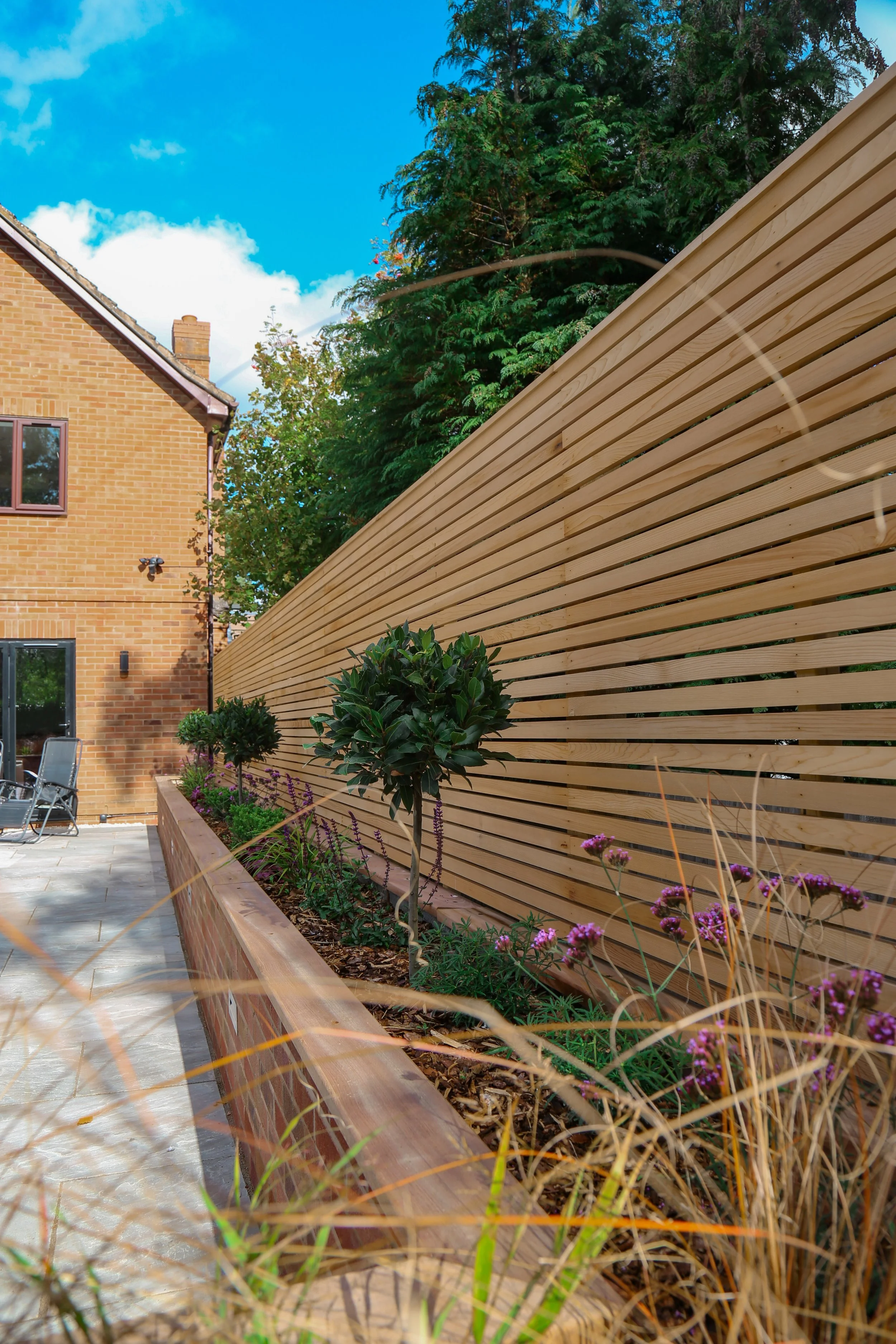 Luxury garden landscaping in Warwickshire, with an entertaining space built, large planting bed, with timber fence and planting.