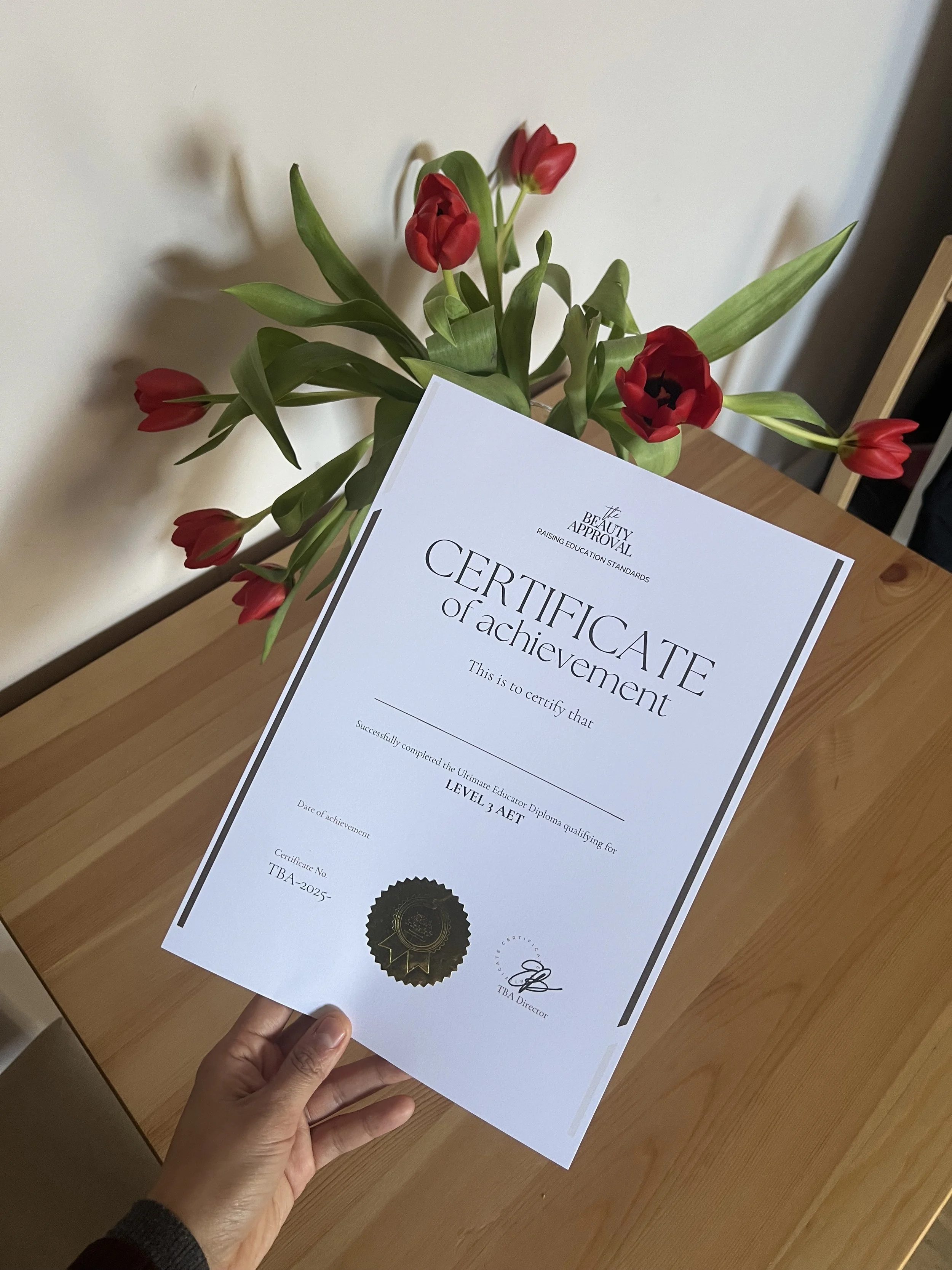 A person holding a certificate of achievement in front of a wooden table and a vase of red and pink tulips.