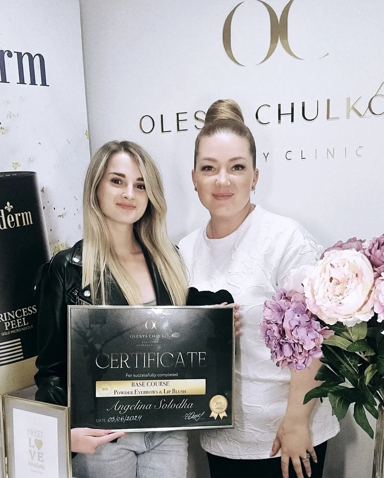 Two women standing together, one holding a certificate. The background features a white wall with gold and black text, including the name Olesya Chulkova. There is a bouquet of pink and purple flowers on the right.