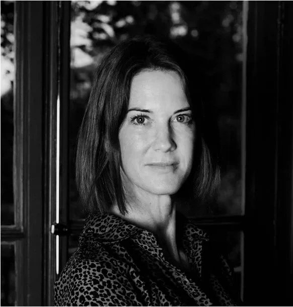 Black and white portrait of a woman with short hair, wearing a patterned shirt, against a blurred outdoor background.