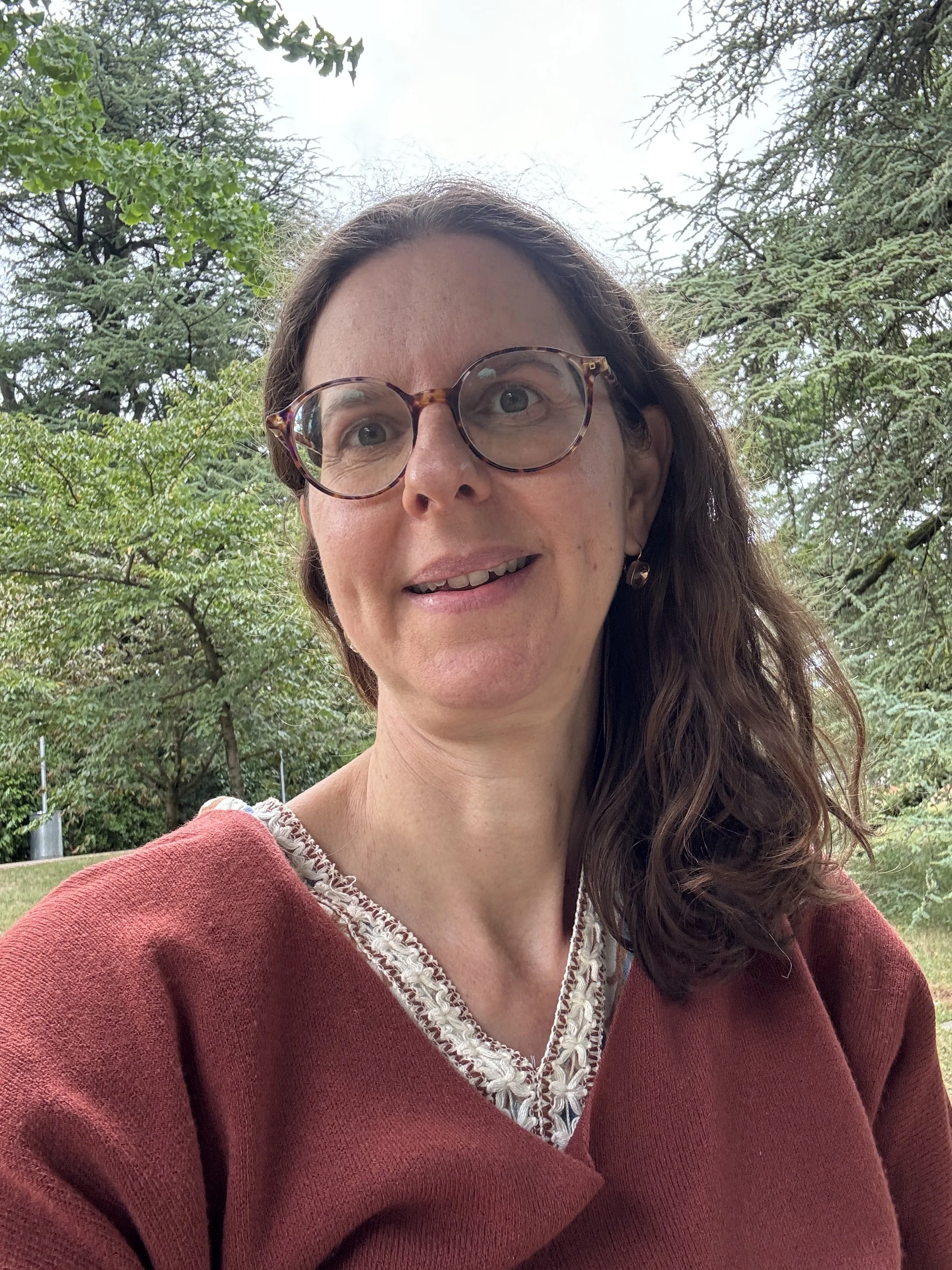 Portrait de Stéfanie Rapillard, médium guérisseuse et communicatrice animalière à Genève, dans une arcade lumineuse avec des arbres en arrière-plan
