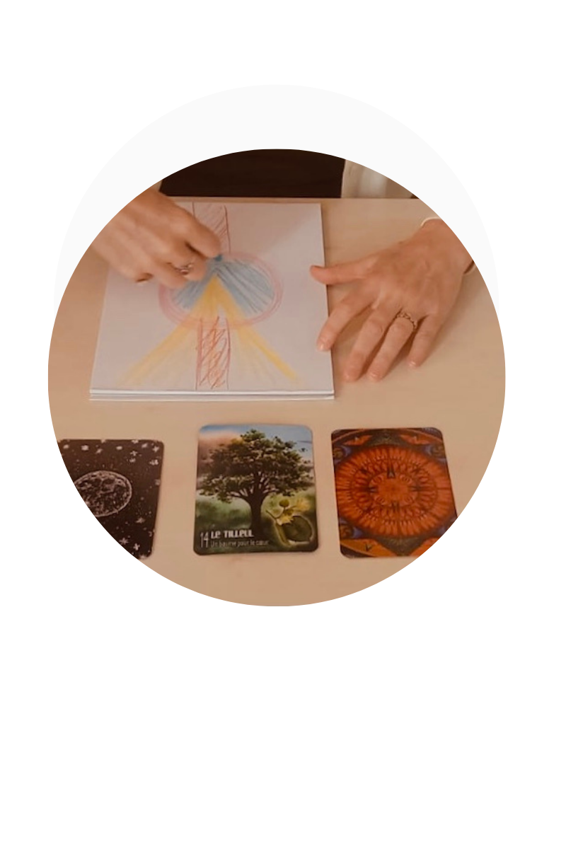 mains qui dessinent en couleur avec trois cartes de cartes oracles posées devant le dessin dans un médaillon rond