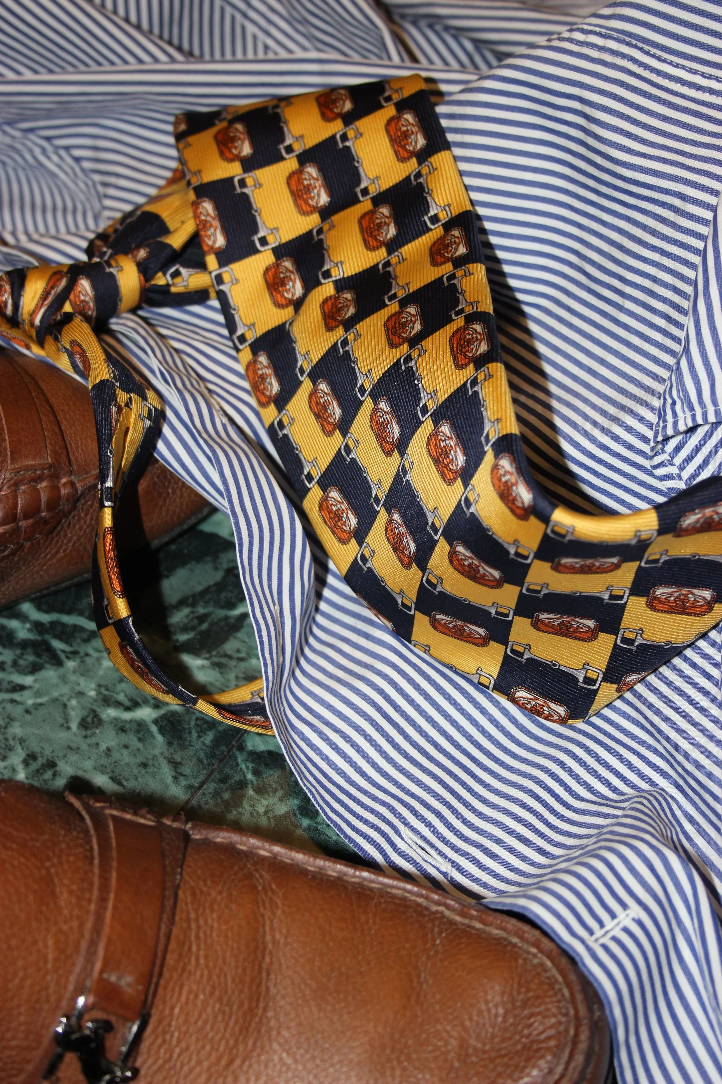 A striped blue and white shirt with a yellow and black patterned tie, a brown leather bag, and a green marble surface.