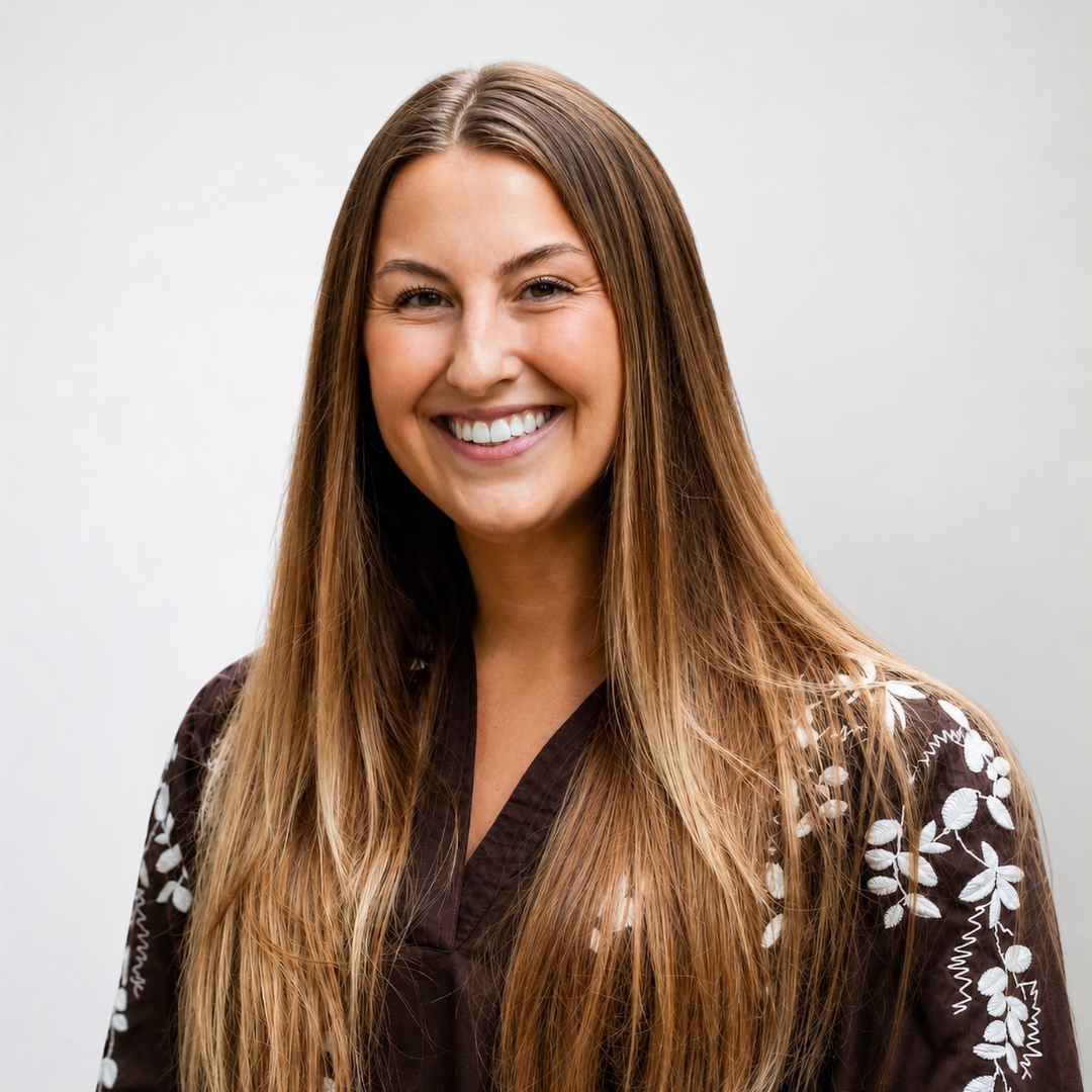 A smiling young woman with brown hair, tan skin, and green eyes, wearing a black blazer and a blue top, against a white background.