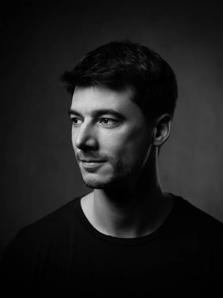 Portrait d'un homme jeune, en noir et blanc, regardant vers la gauche, avec une expression neutre, portant un t-shirt noir.