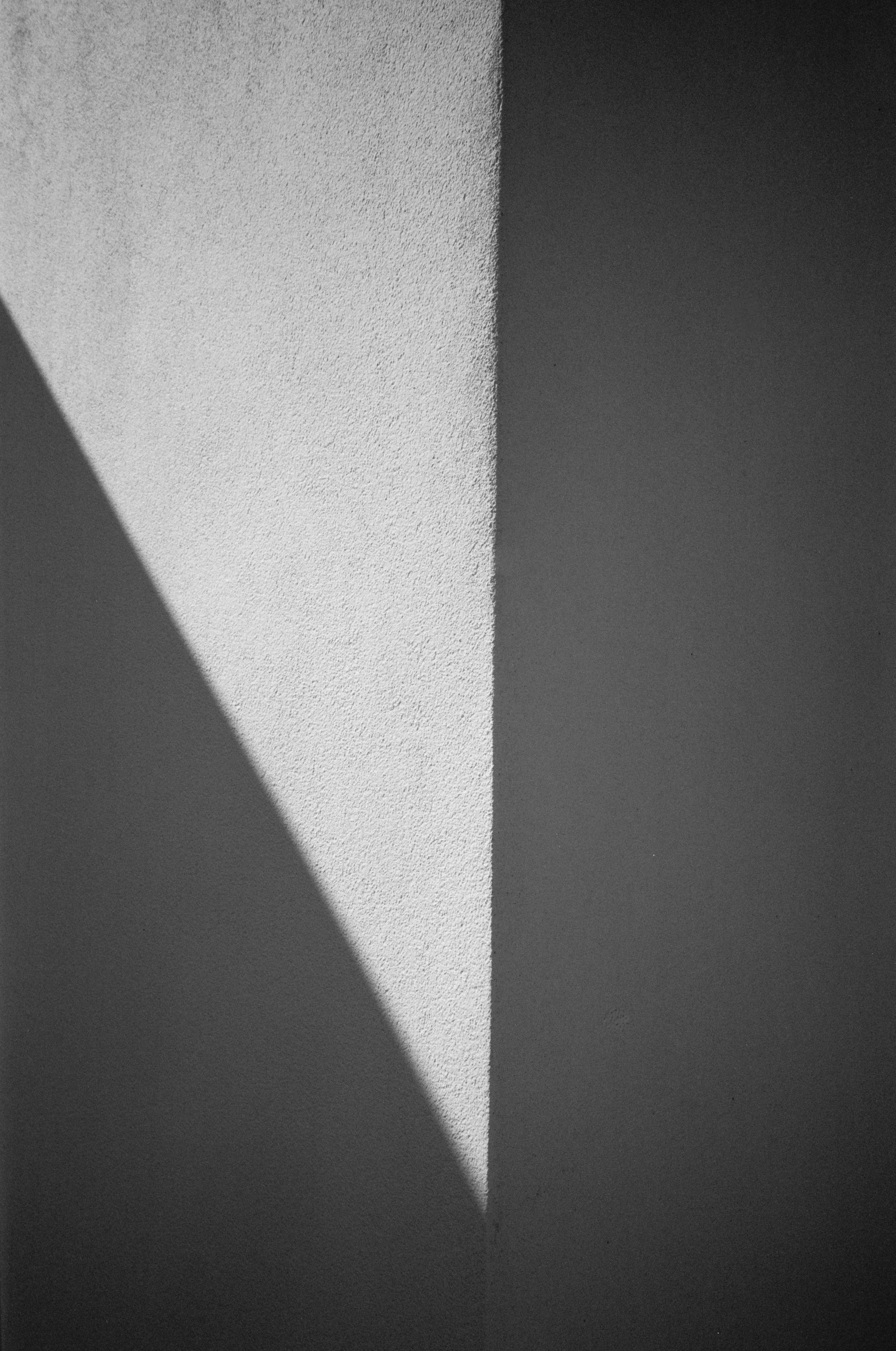 Abstract black and white photo of a corner where two textured walls meet, with shadows creating geometric shapes.