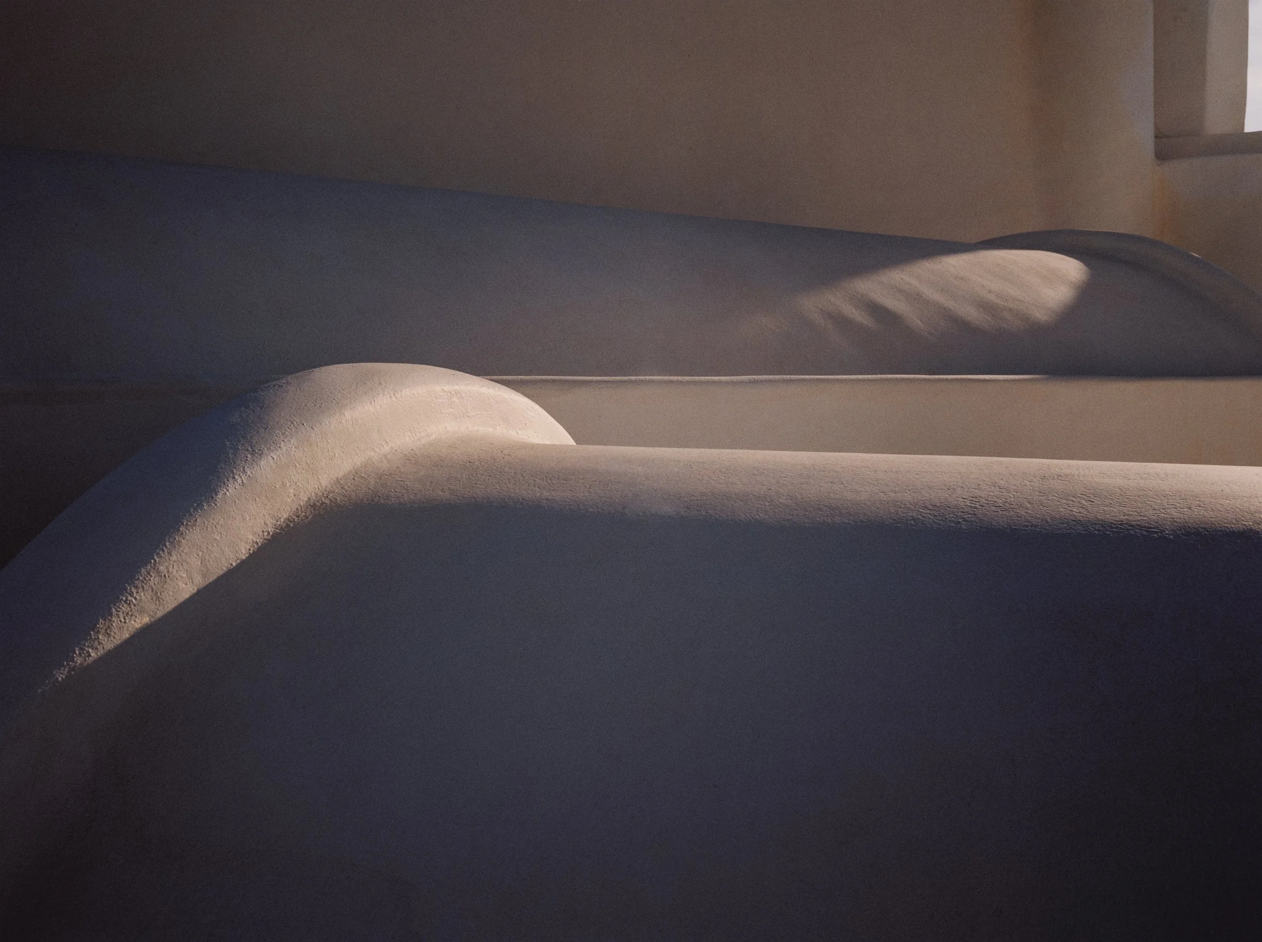 Close-up of smooth, white, snow-covered surfaces with soft shadows in a minimalist indoor space.