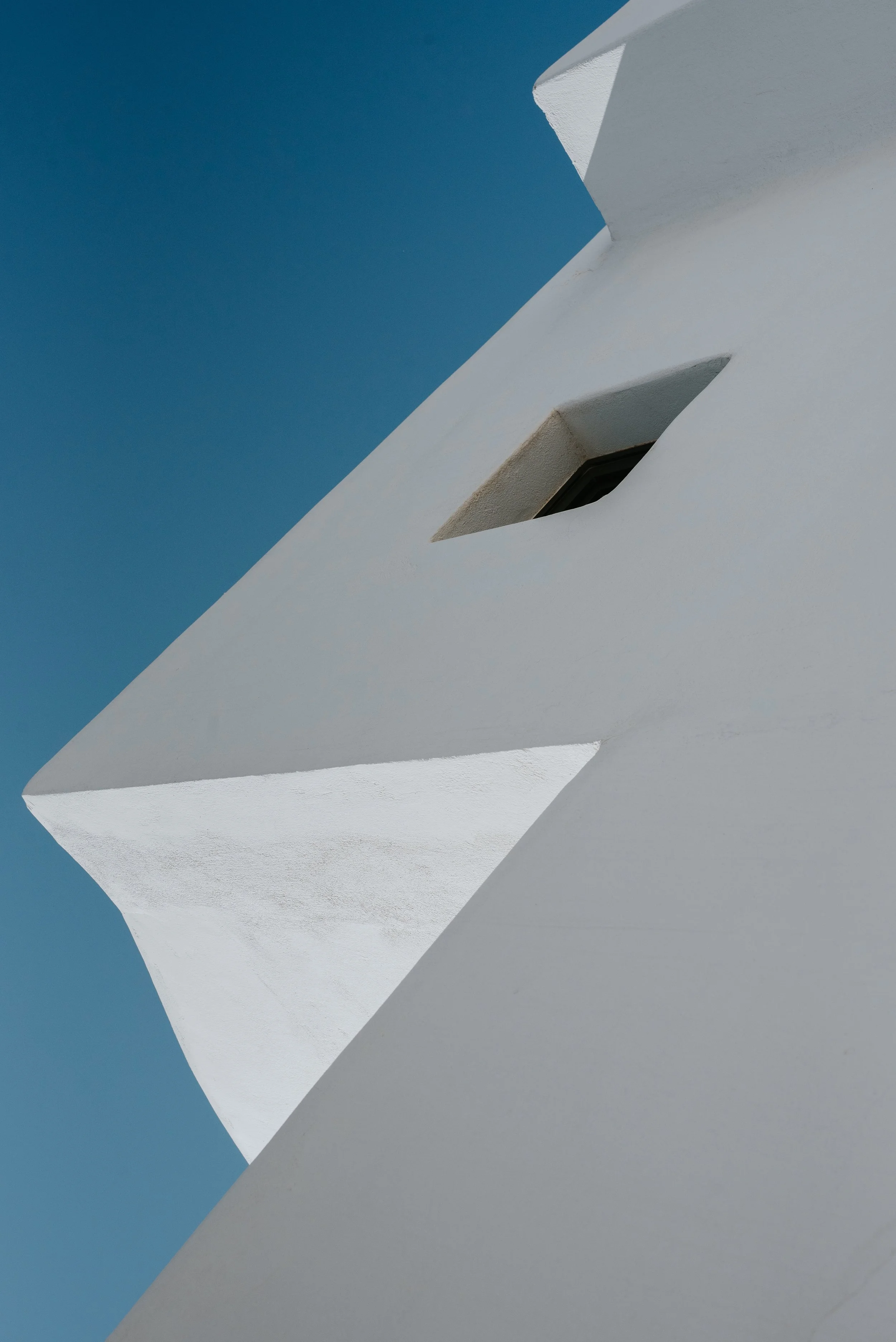 Close-up of a white modern building with angular design and a small window against a clear blue sky.