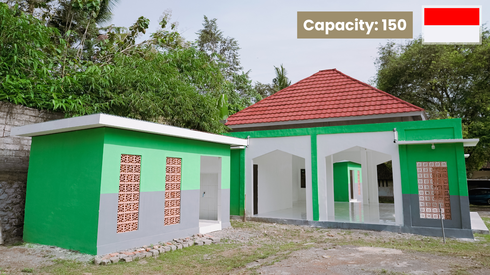 A small, modern building with a conical roof, green and white walls, and decorative windows, surrounded by a concrete pavement and trees in the background.