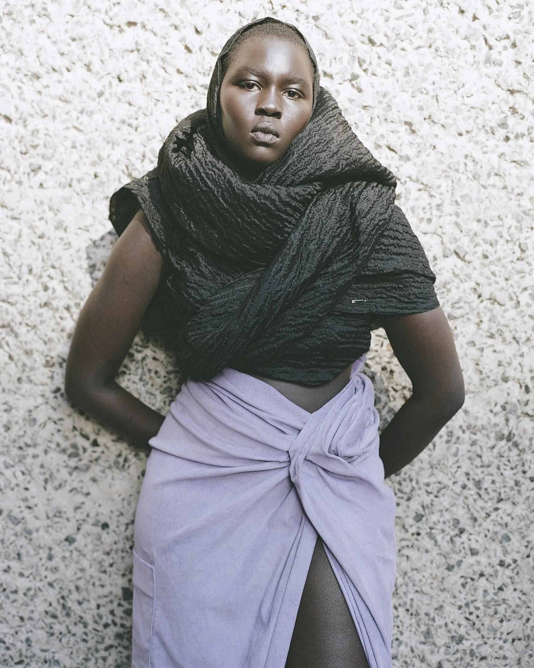 Frau liegt auf einem weiß-braunen Teppich, trägt einen schwarzen Schal und einen lila Rock