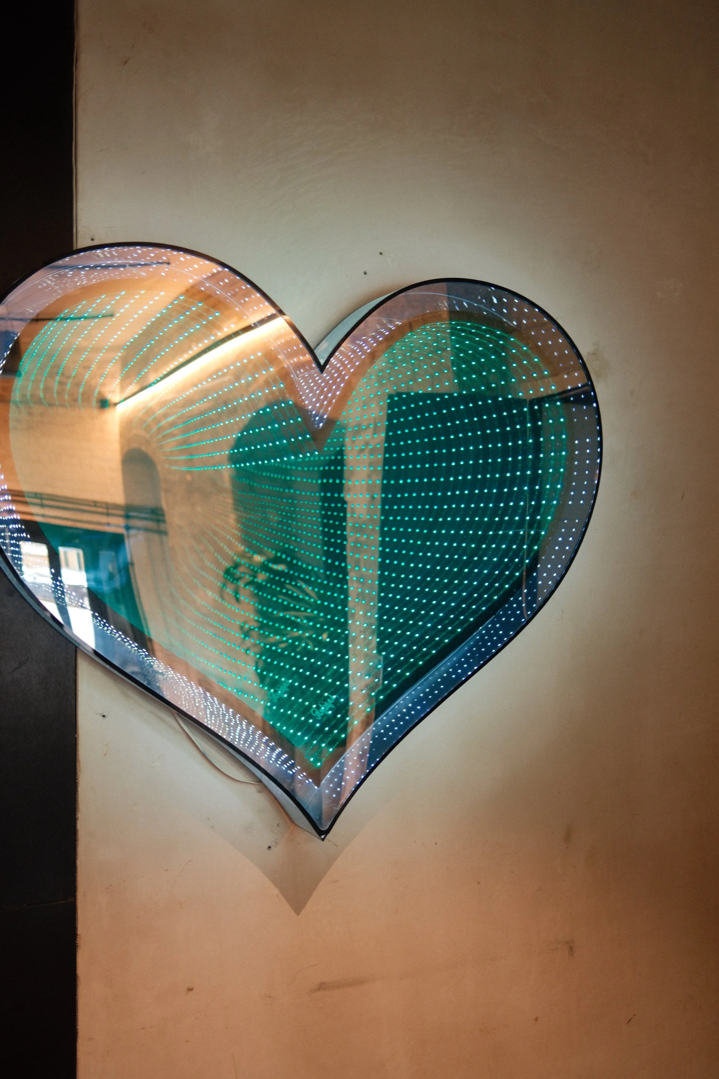 A heart-shaped LED light with green and white lights, reflected on a surface.