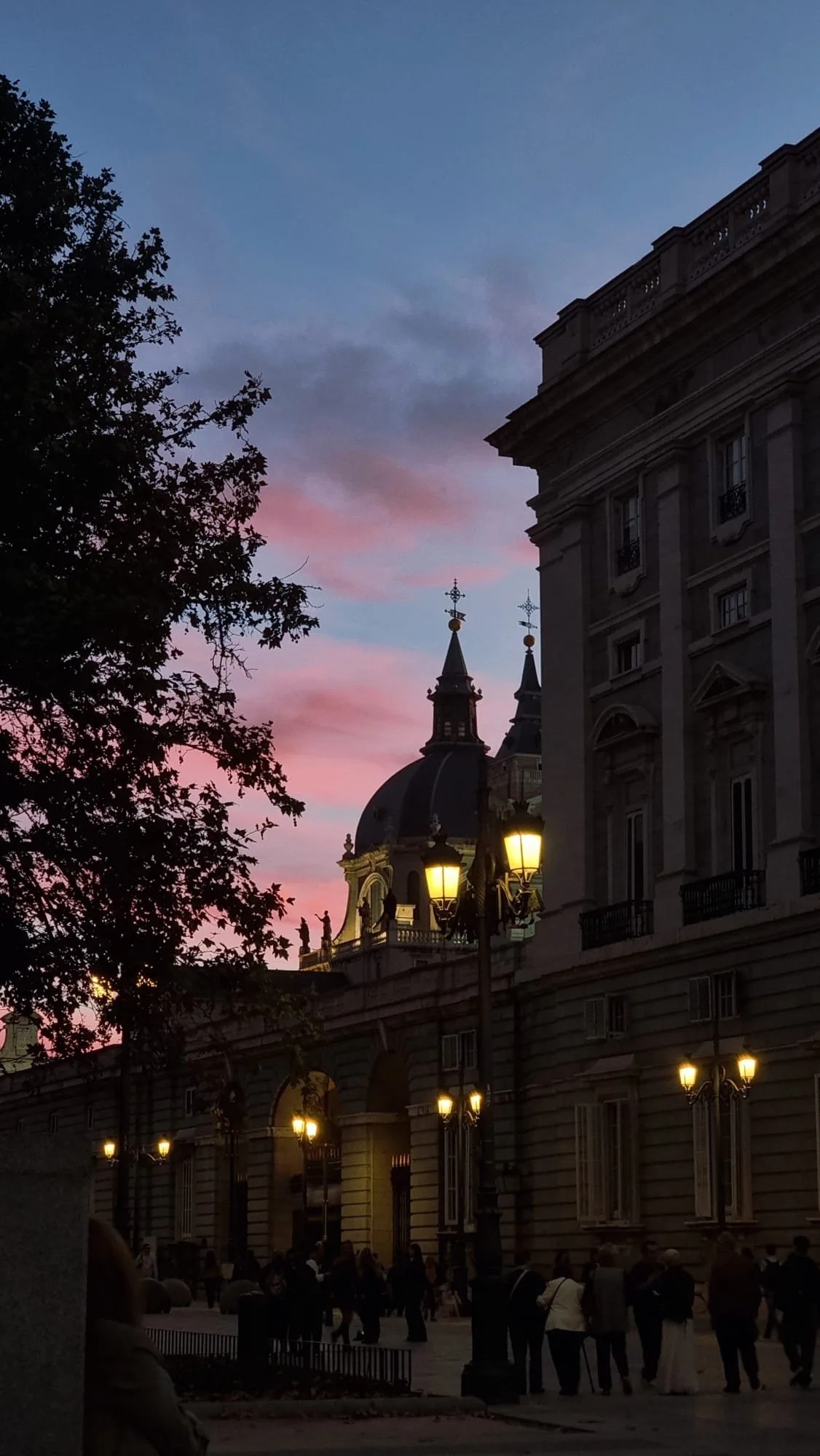A city street at dusk with historic buildings, lamp posts, and pedestrians, and a colorful pink and blue sky. Madrid yoga retreat weekend meet-up group meala soul