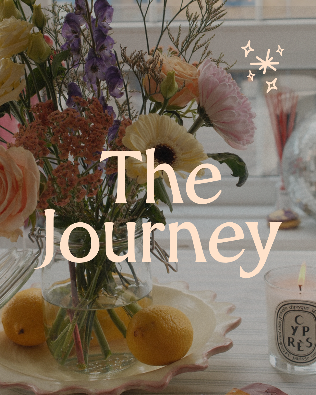 A vase of mixed flowers on a table with lemons and a lit candle in the foreground and a window in the background with the text 'The Journey' overlaid.